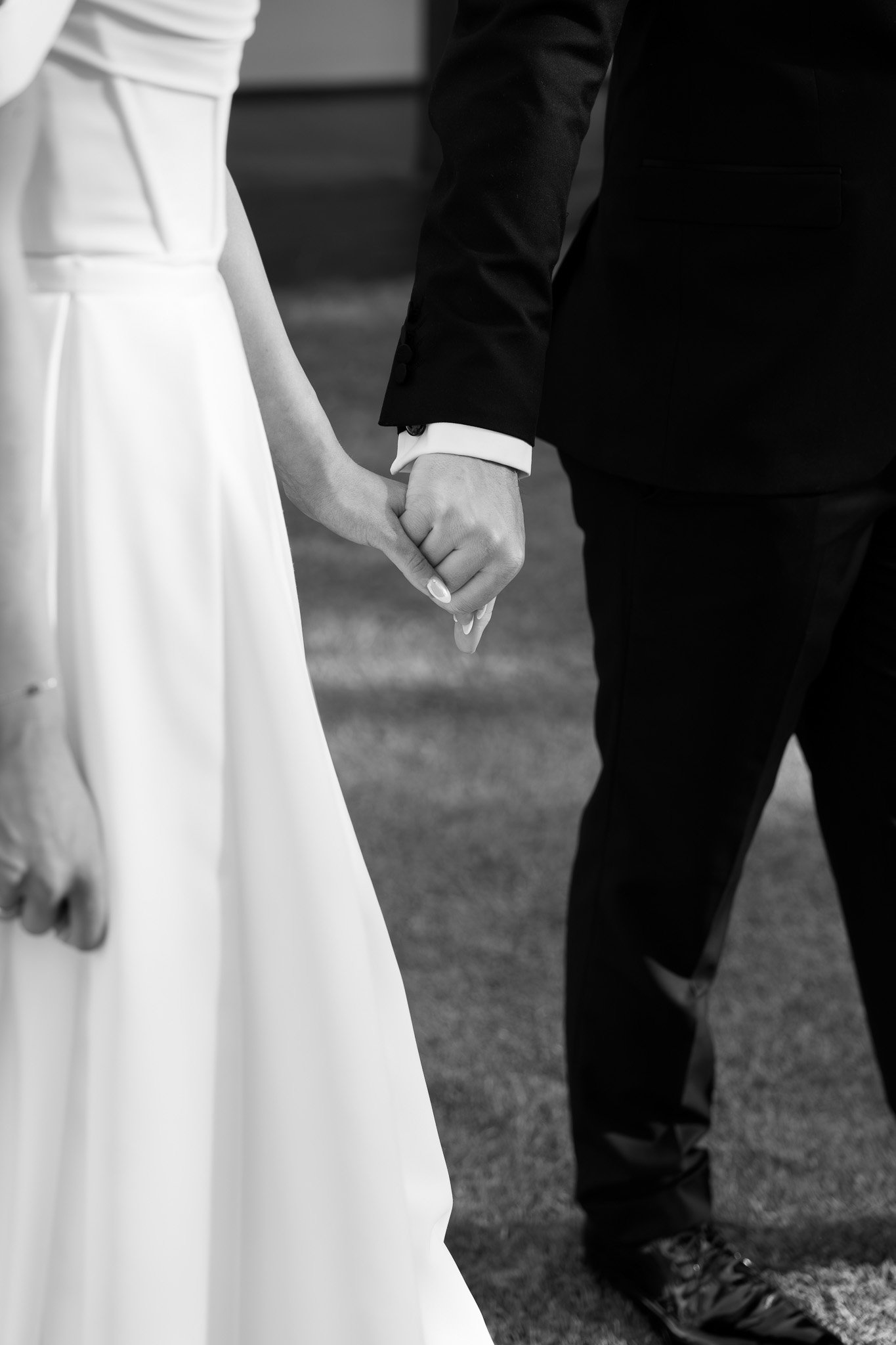 A bride and groom holding hands during their wedding ceremony, dressed in formal attire, black and white photo.