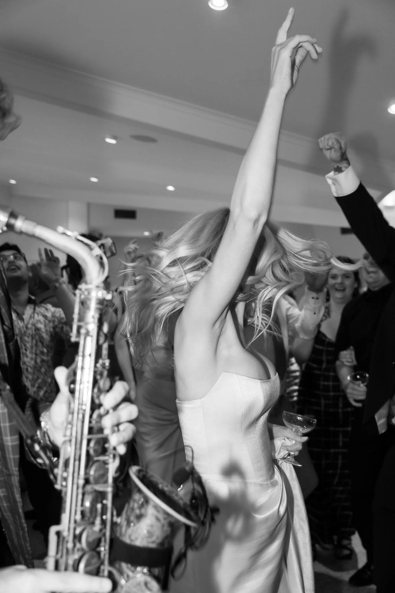 A woman in a satin dress dancing at a lively party with a band playing, surrounded by guests.