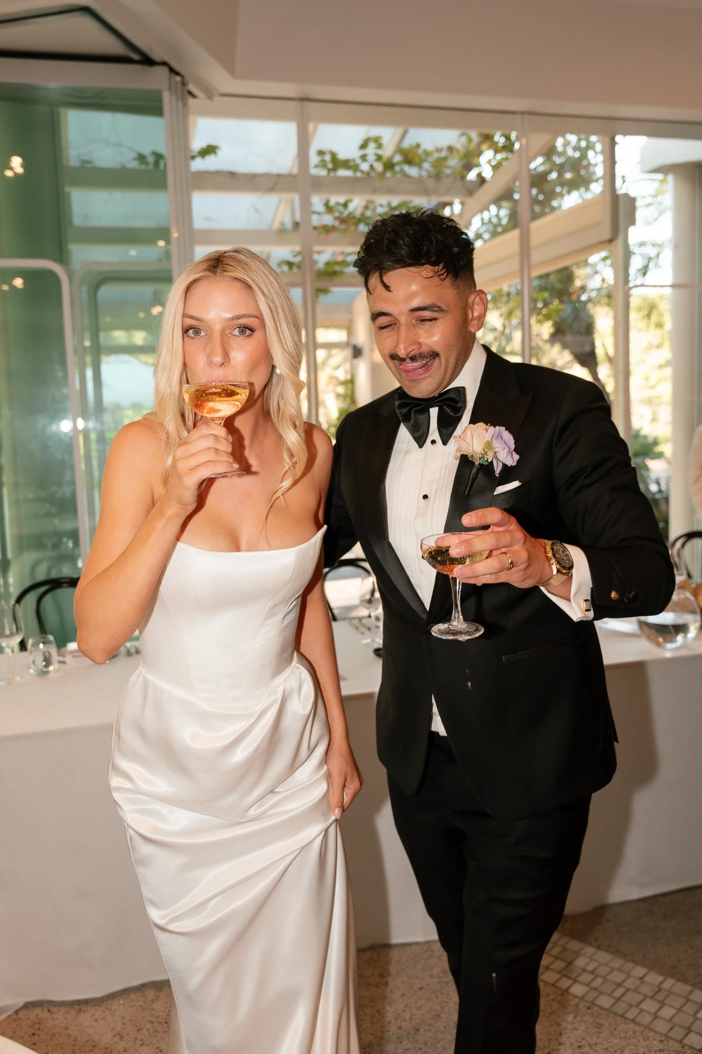 A bride and groom at a wedding reception, holding glasses of champagne and appearing to enjoy themselves.