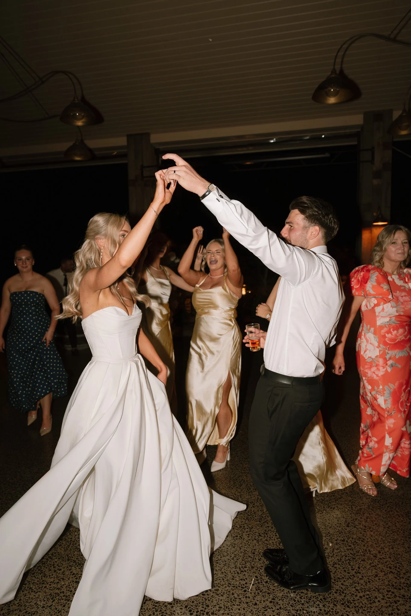 Couple dancing at a celebration with other women in dresses in the background.
