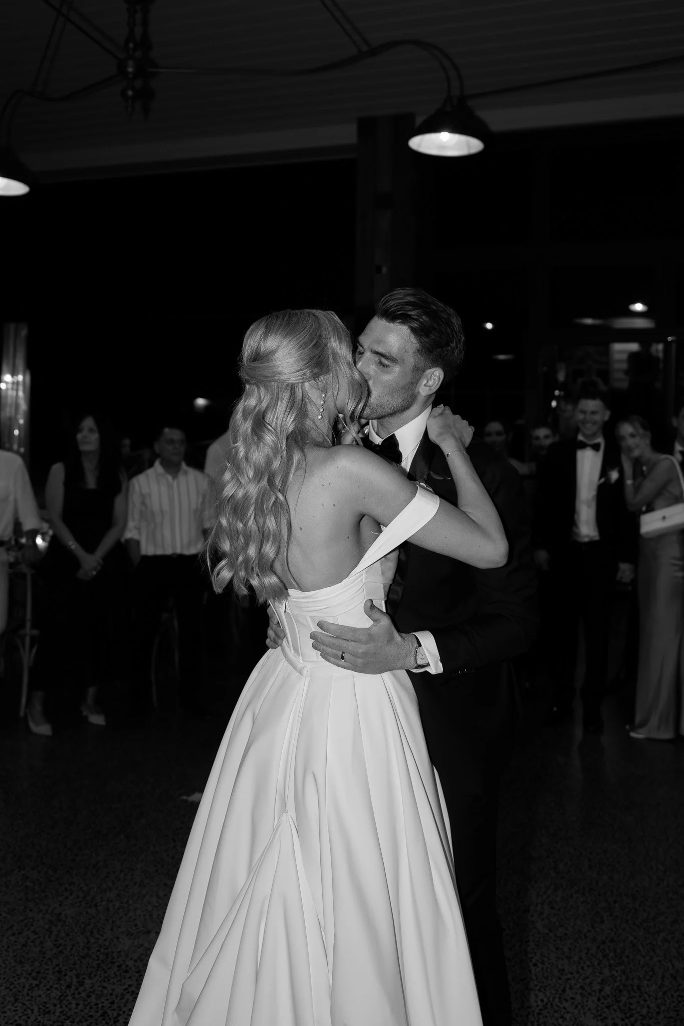 A bride and groom share a dance at their wedding reception, surrounded by guests.