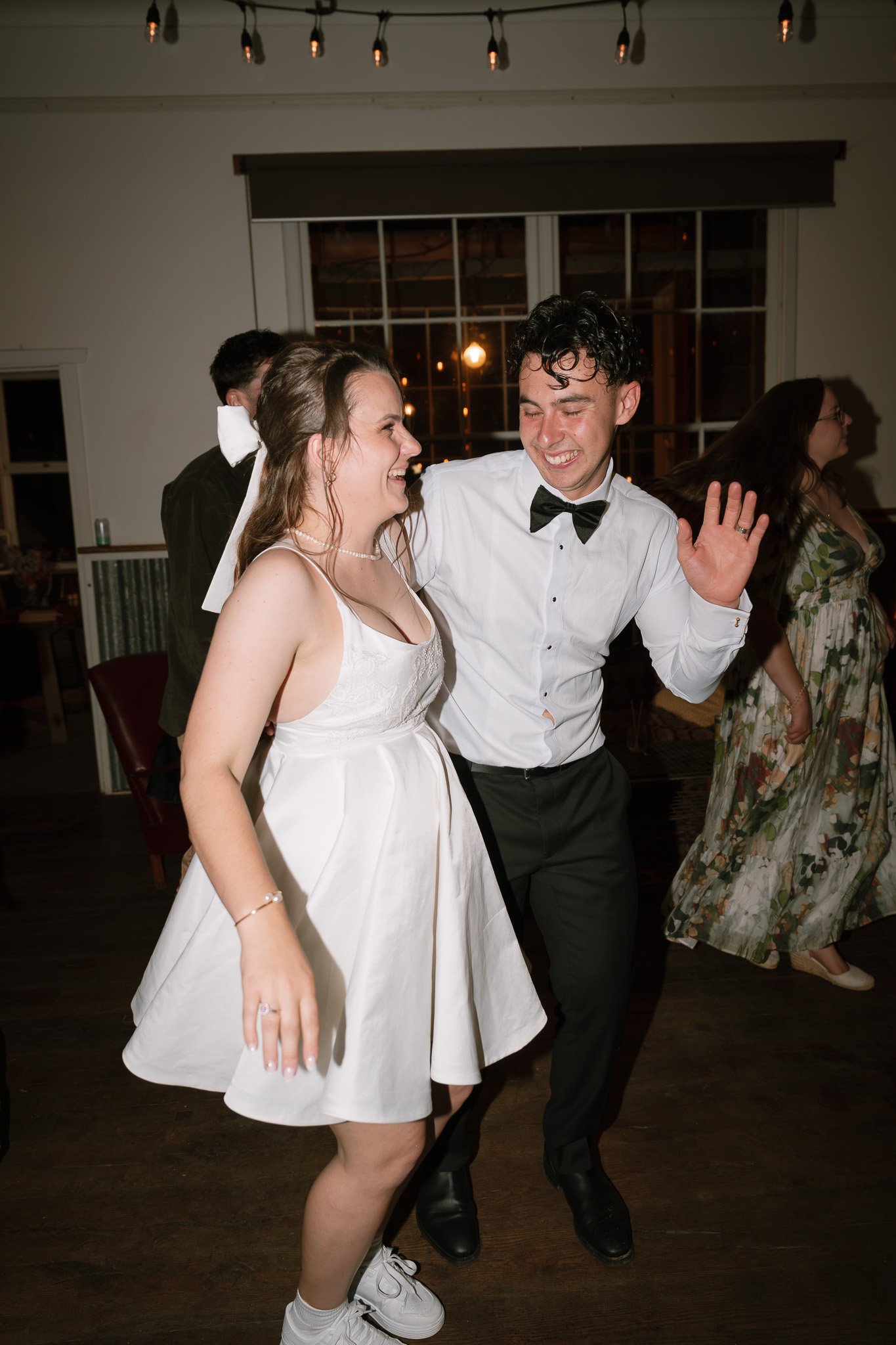 A young woman in a white dress and a young man in a tuxedo dancing and smiling at a wedding reception.