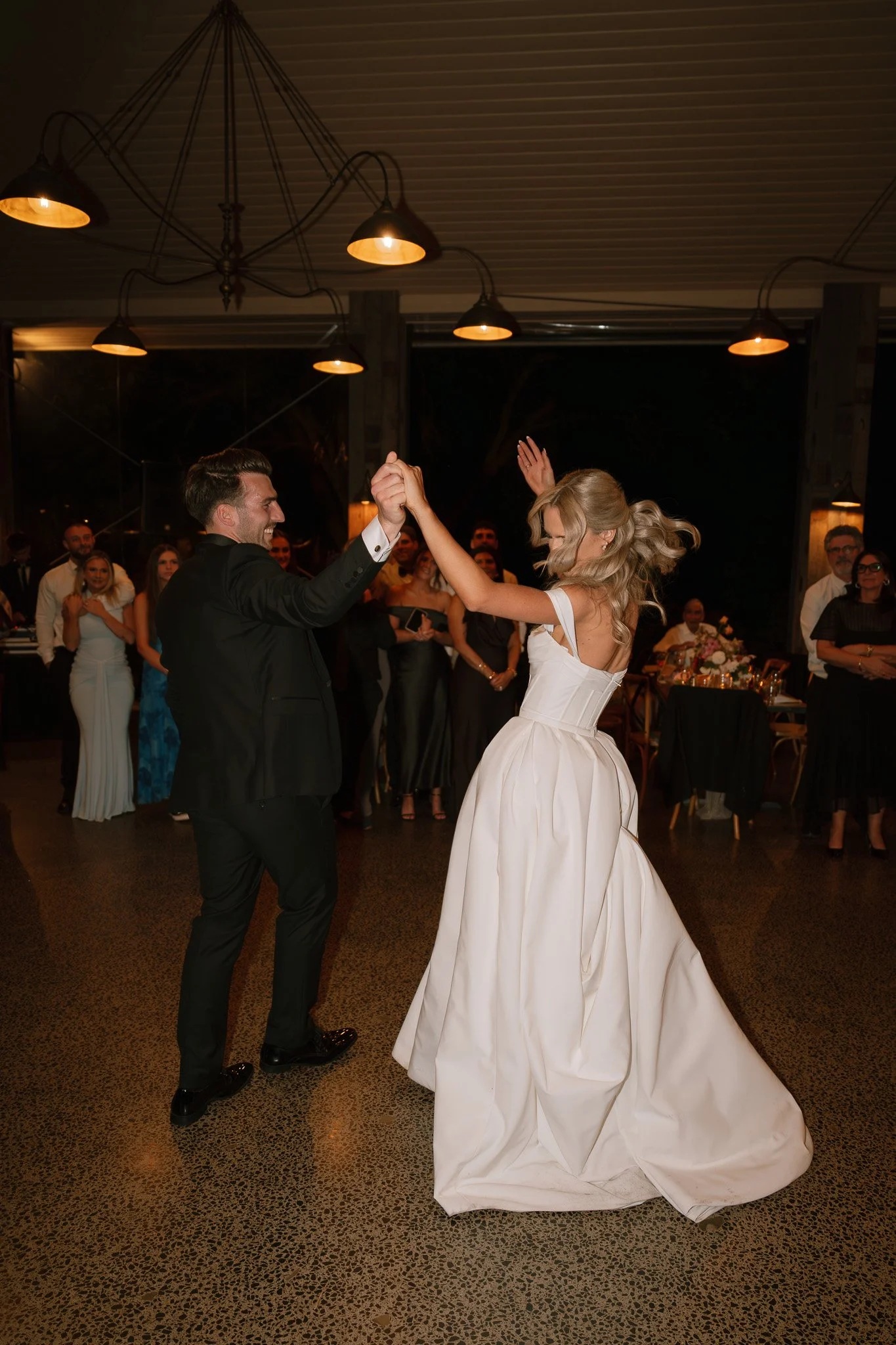 A bride and groom dancing at their wedding reception with guests watching in the background.