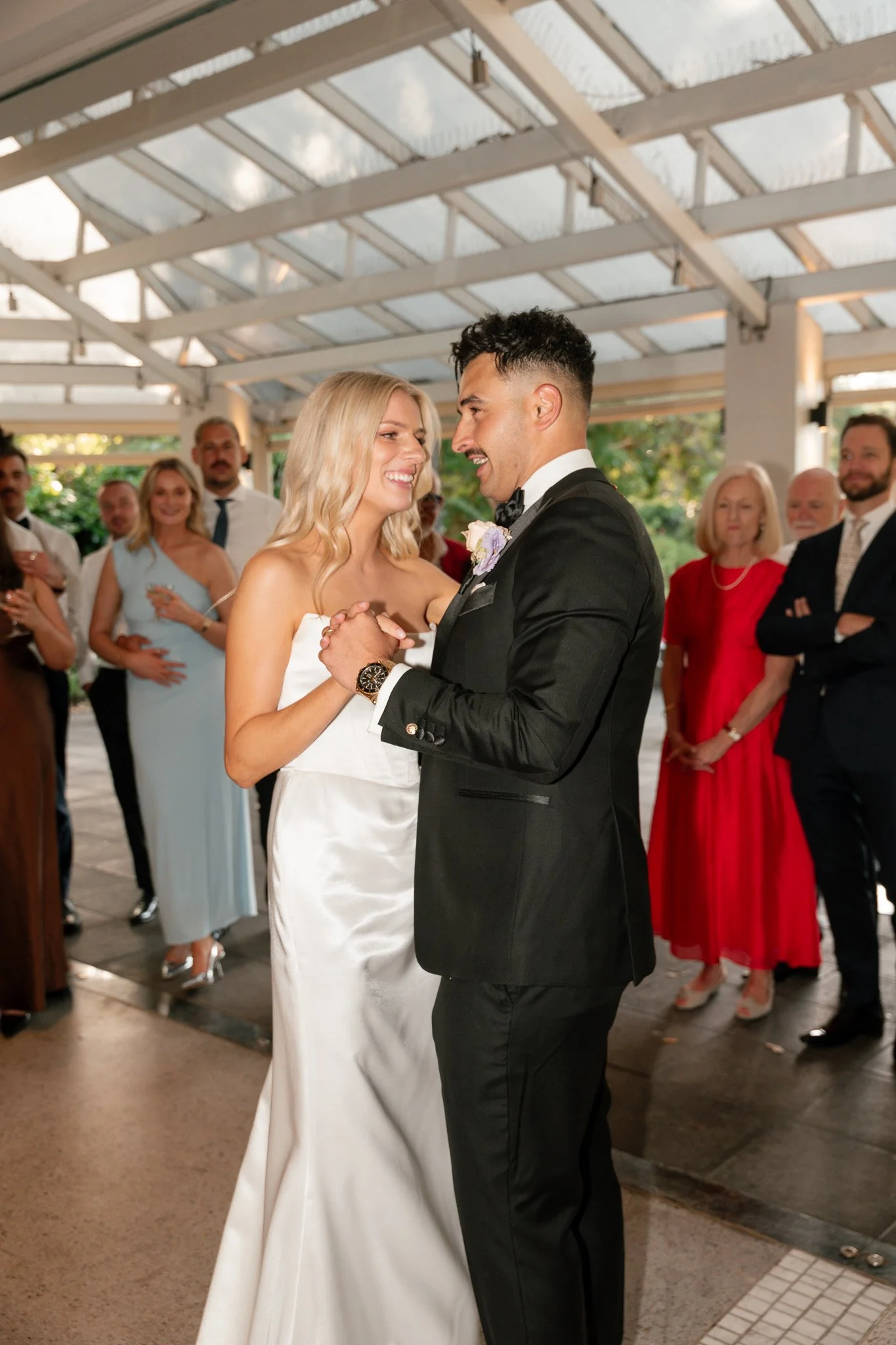 A bride and groom dance at their wedding reception, surrounded by guests in a covered outdoor venue.