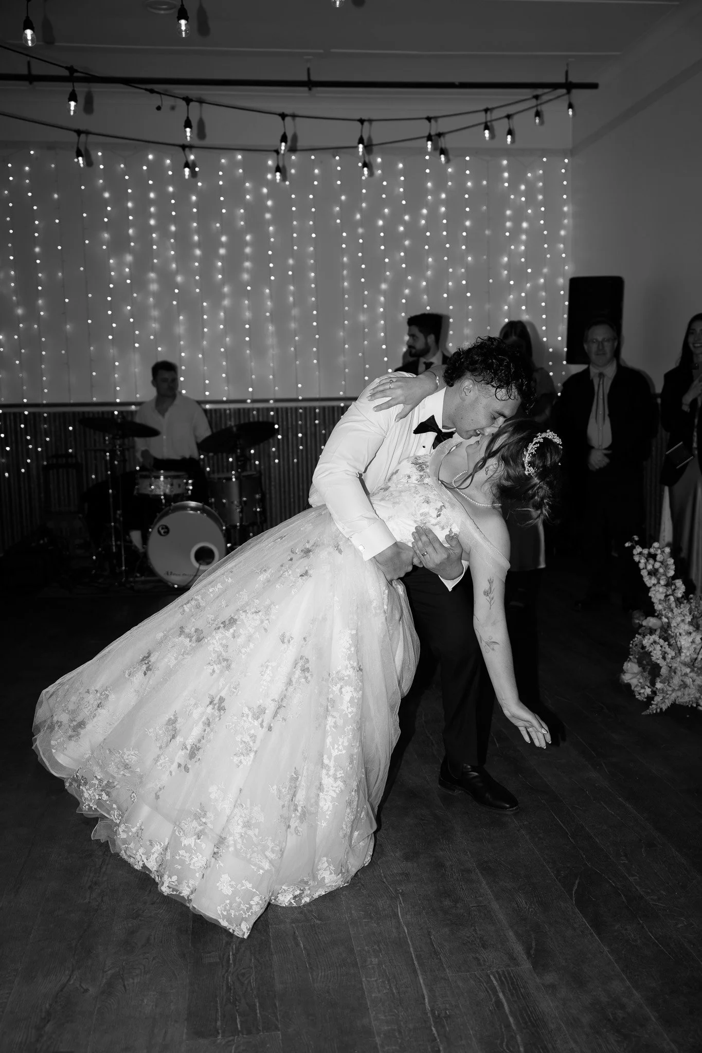 A bride and groom dance at their wedding reception, with a draped curtain of string lights and a band playing in the background.