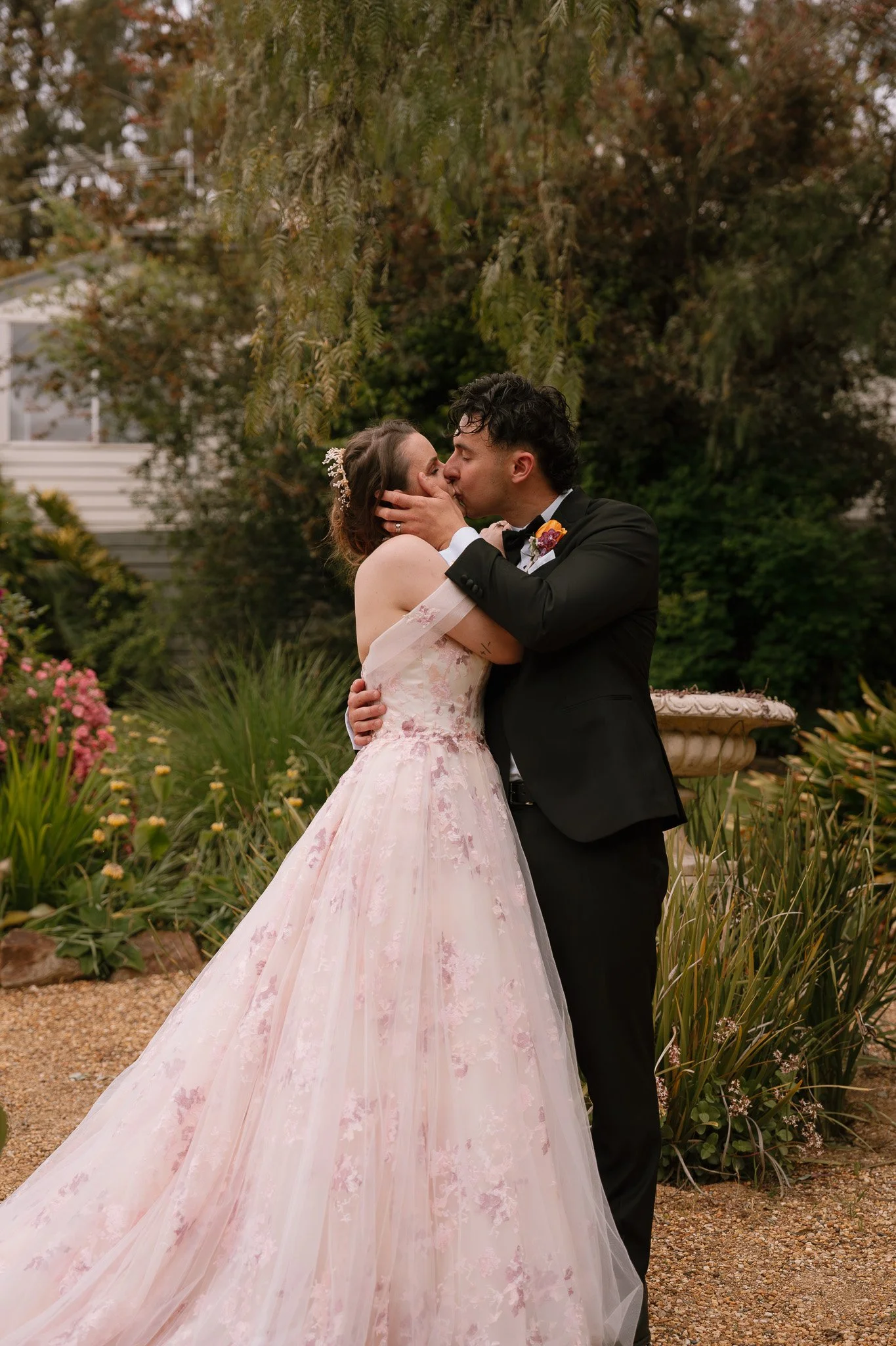 A couple kissing at their wedding outdoors, with greenery and flowers in the background.