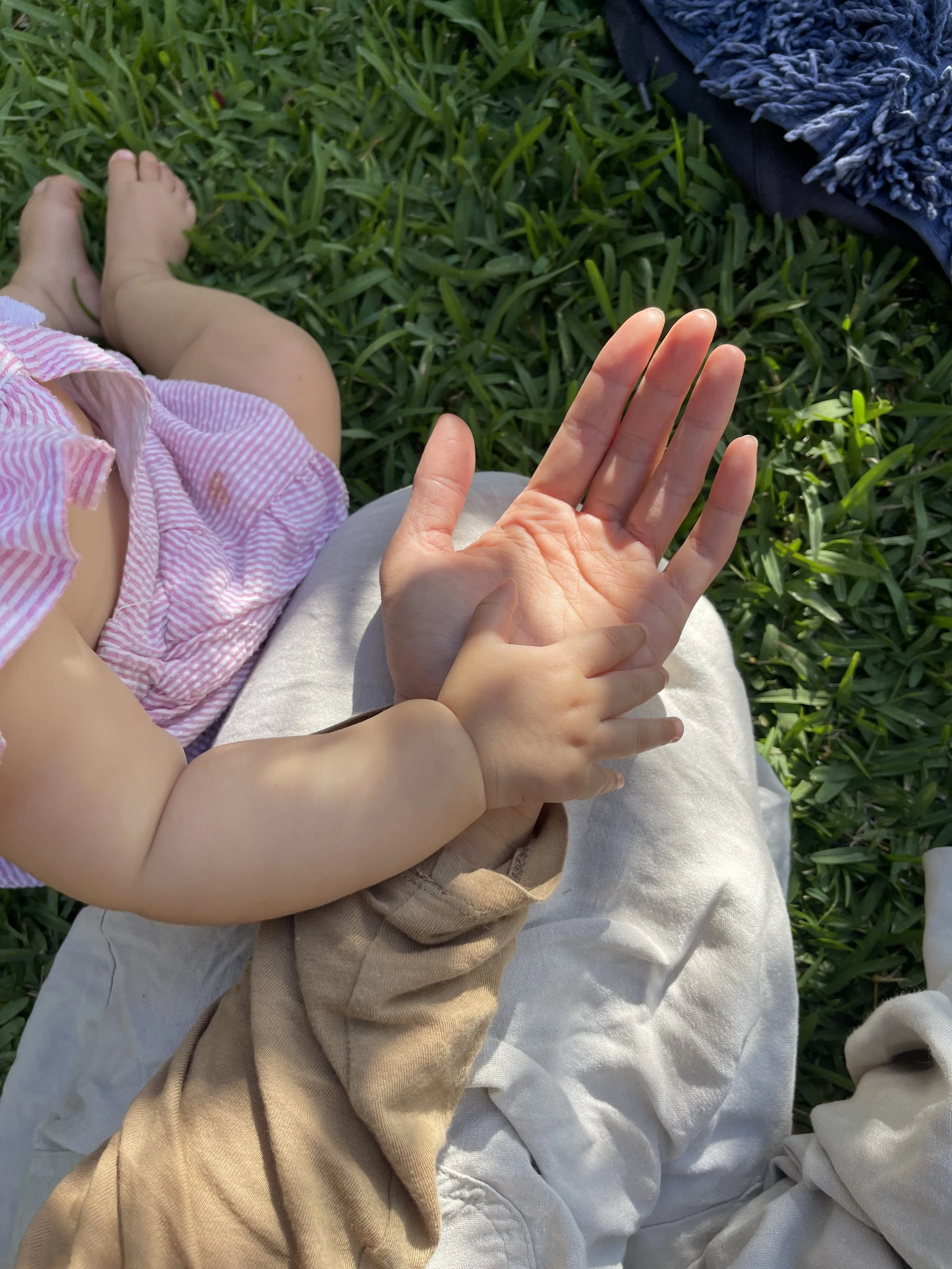 A child holding an adult's hand while sitting on grass outdoors.