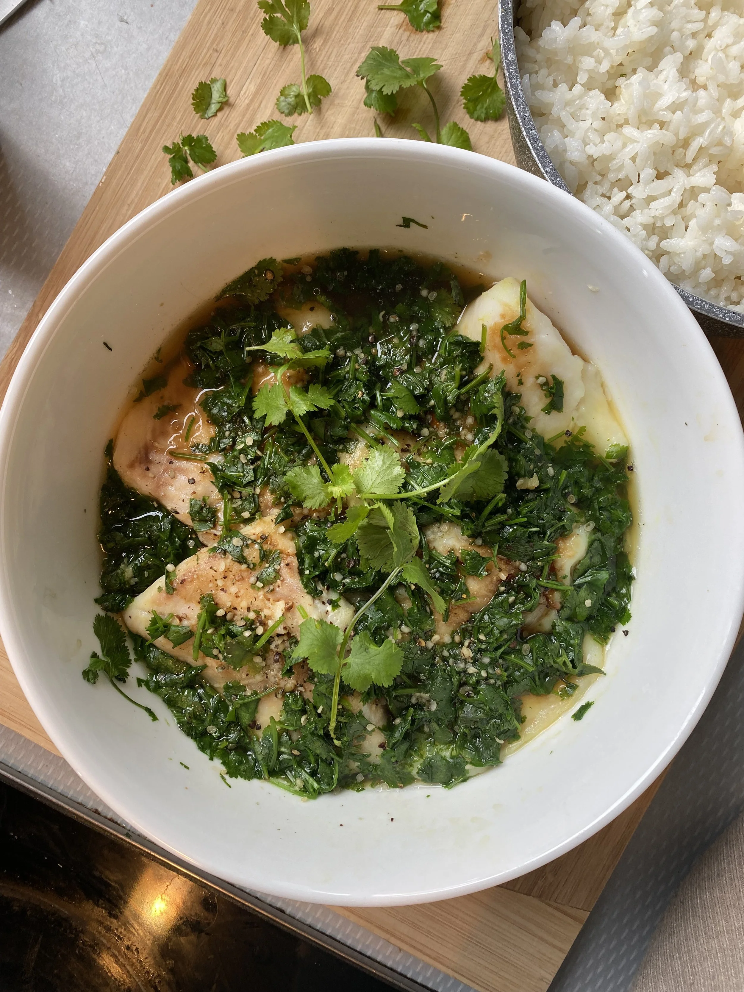 A bowl of poisson with herbs and seasoning, served with a side of white rice.