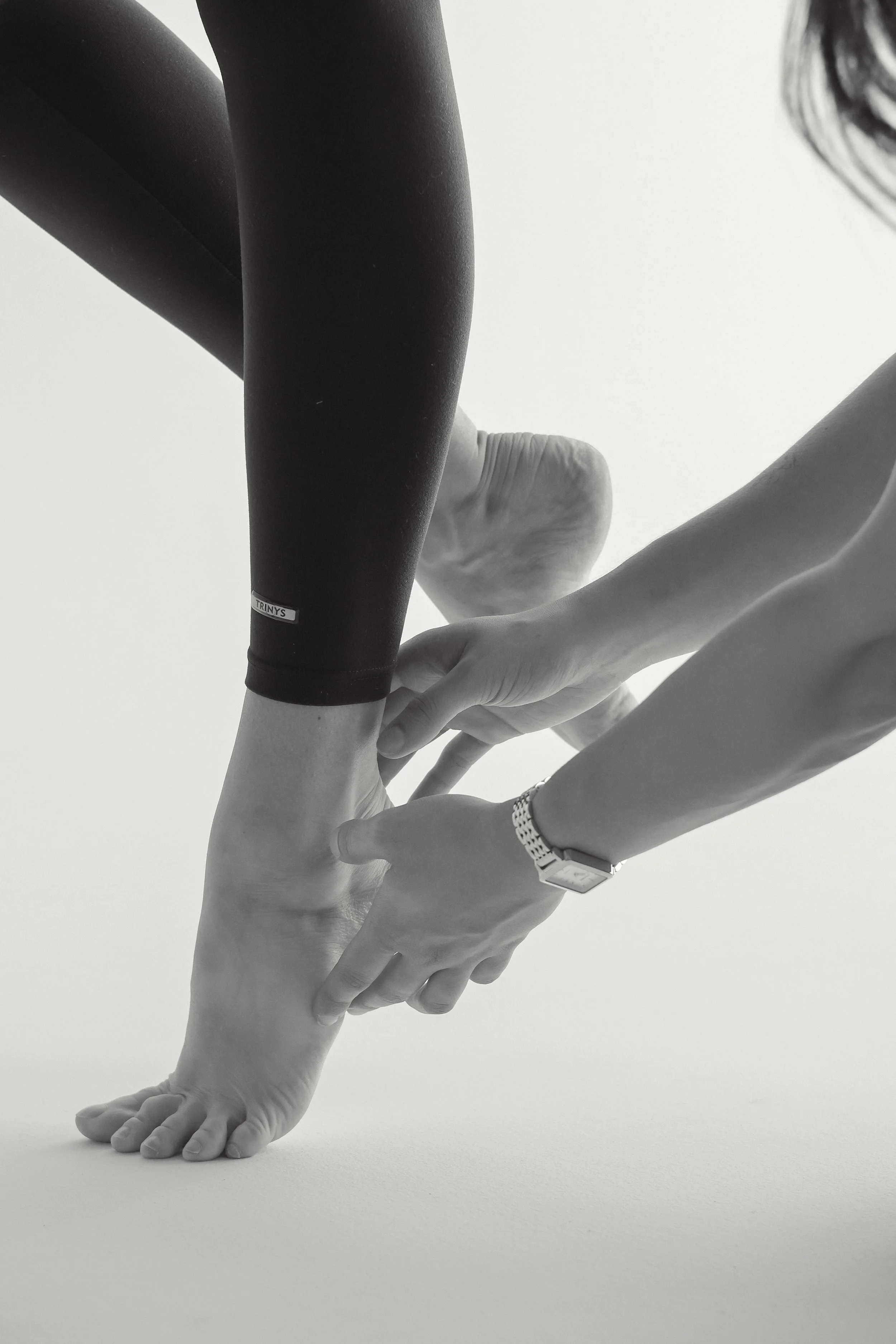 A dance physiotherapist is kneeling on the ground assessing a dancer who is performing a single-leg heel raise.