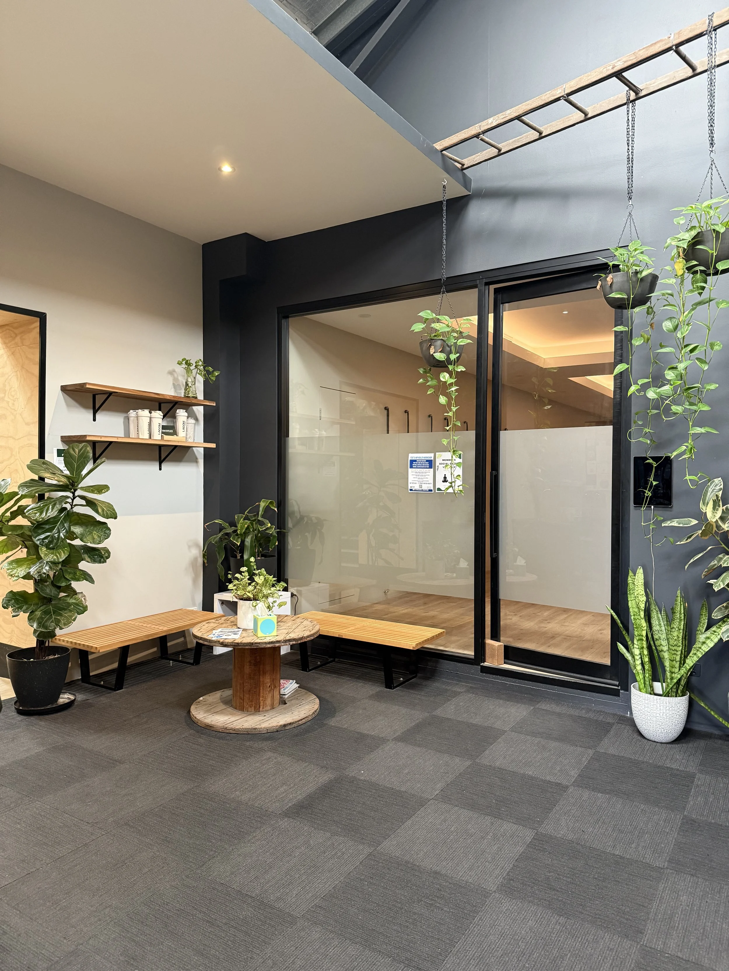 The waiting room of Newcastle Dance Physiotherapy. Two benches and a round table surrounded by plants.