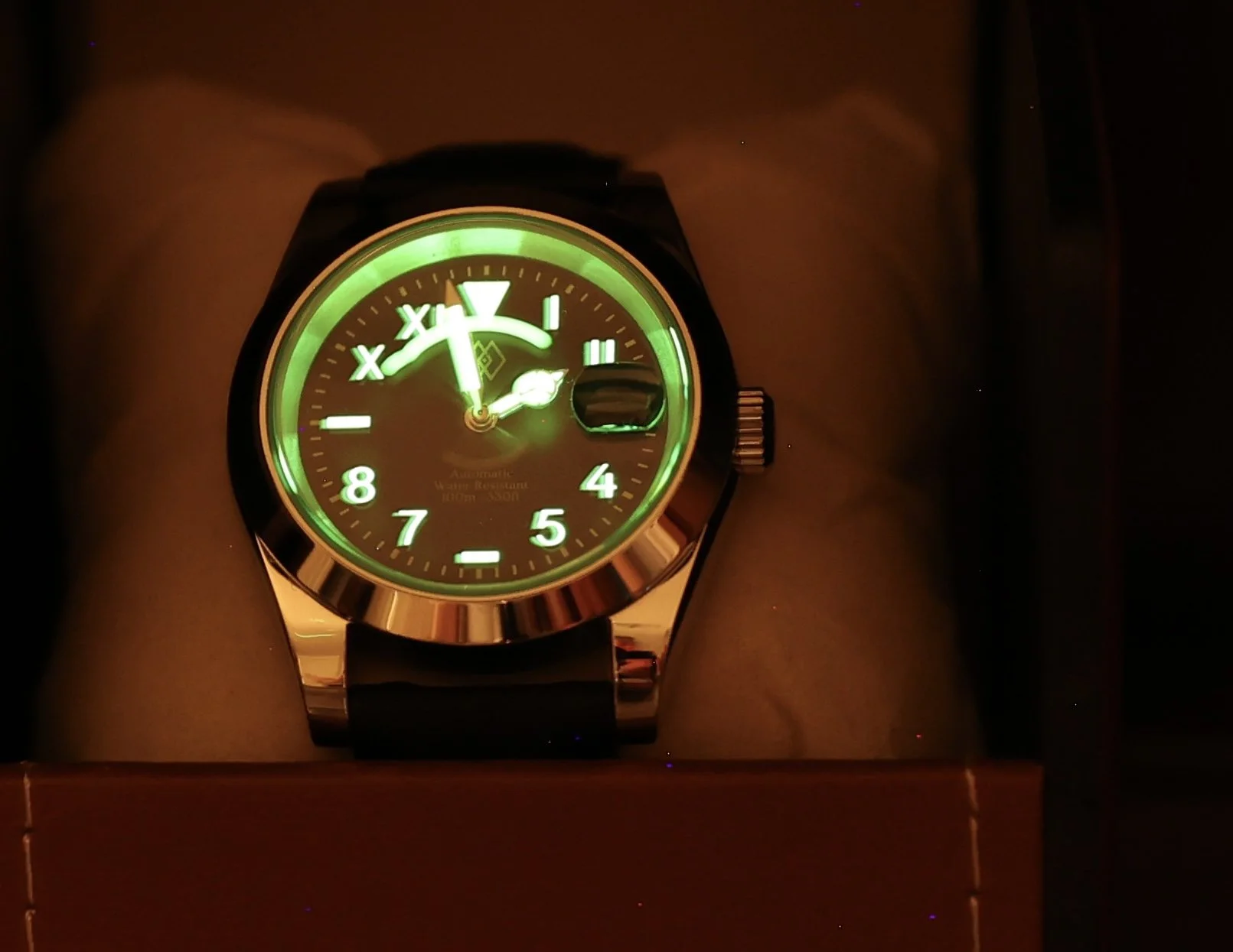 Luminous wristwatch with a black band and a round face displaying the time at 4:02, featuring a glow-in-the-dark dial with green luminous markings and hands, and a small date window.