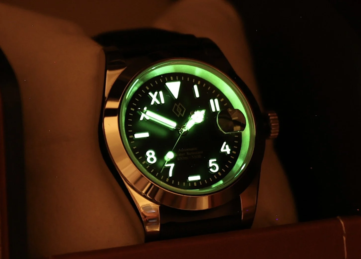 A wristwatch with a green glow in the dark, showing the time as approximately 7:55, with luminous Roman and Arabic numerals on the dial.