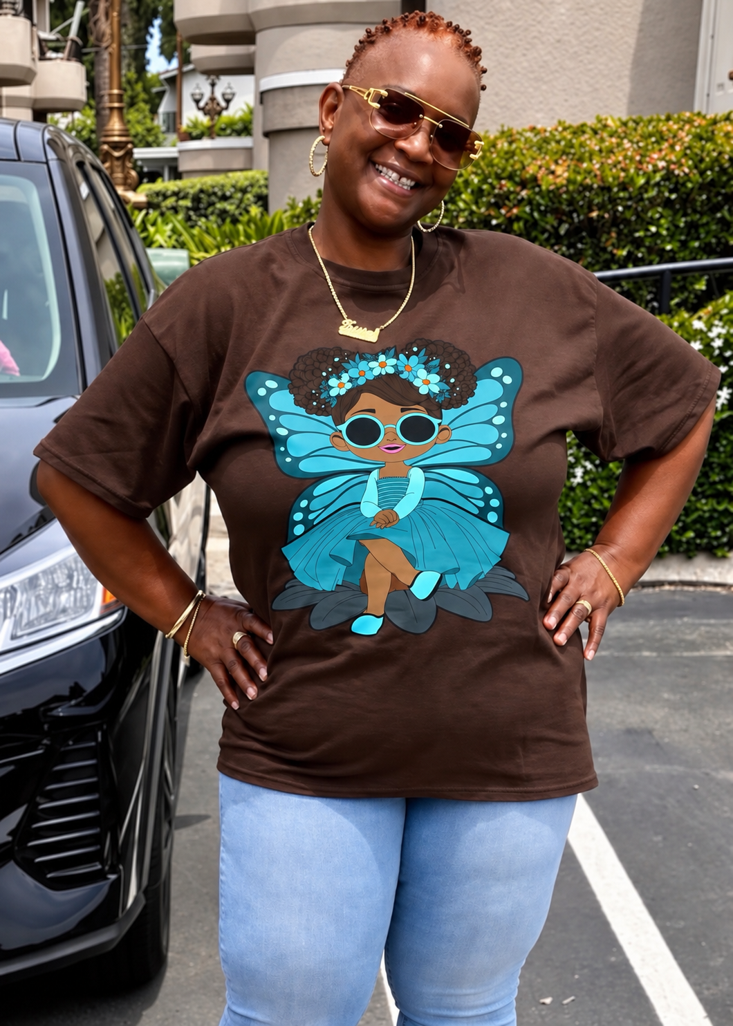Black woman posing with hands on her hips and a big smile while wearing her brown Sassy Sammy Pixie Signature Shirt - Coco Pixies Character Graphic T-Shirt, ADULT SIZE