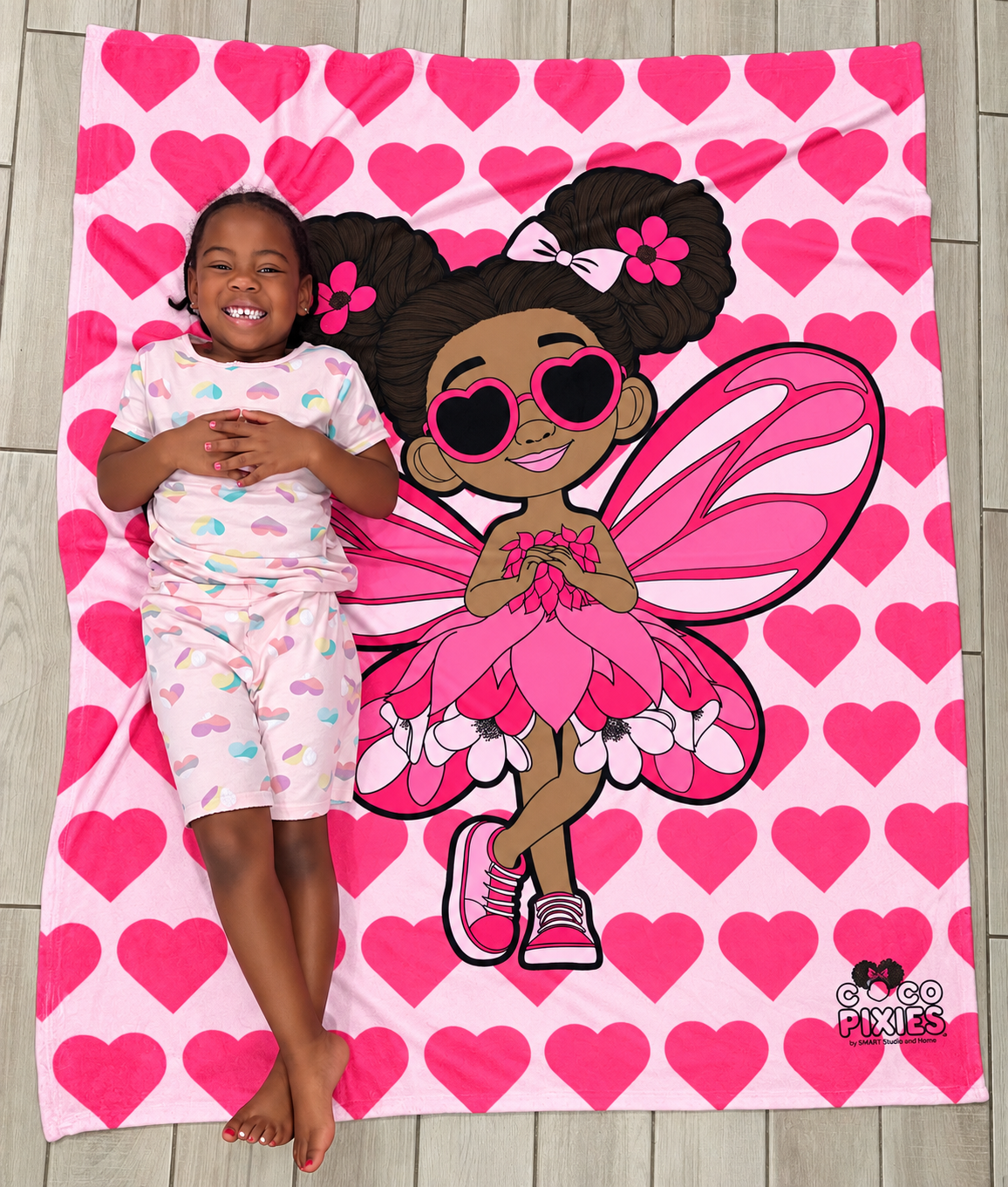 Little girl laying on her Glitzy Gracelynn Pixie Velveteen Plush Blanket - Coco Pixies Bubblegum Pink Signature Heart Pattern Throw, 50" x 60"