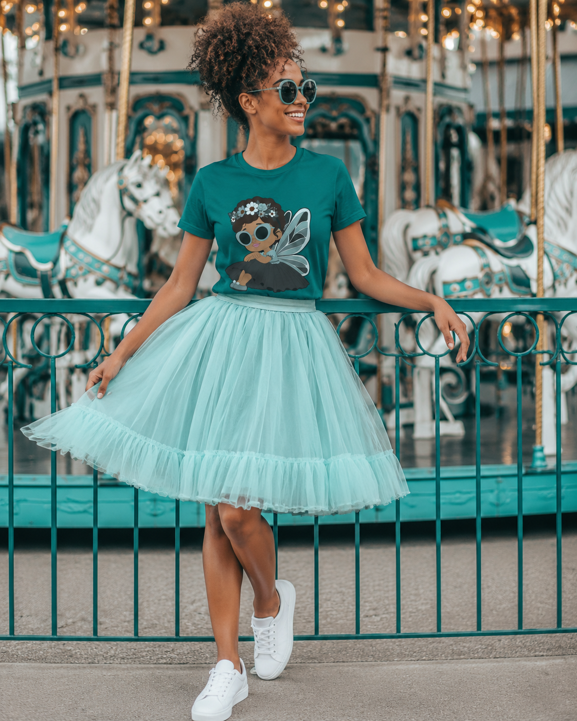 Black woman wearing a teal Coco Pixies Pixie Piper T-shirt with an aqua tulle skirt and white sneakers beside a carousel.