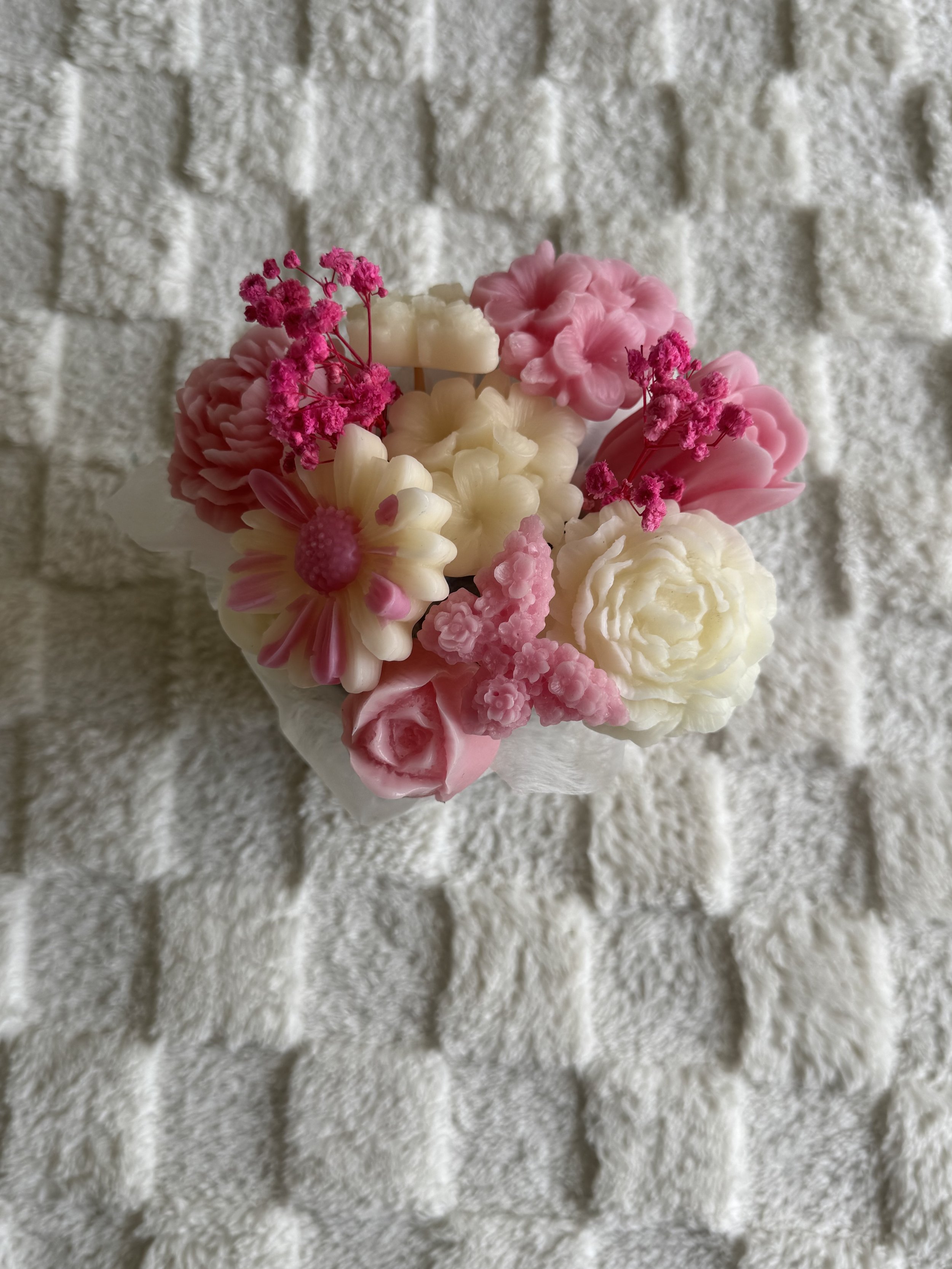 A bouquet of pink and white artificial flowers with pink baby's breath, placed on a textured white surface.