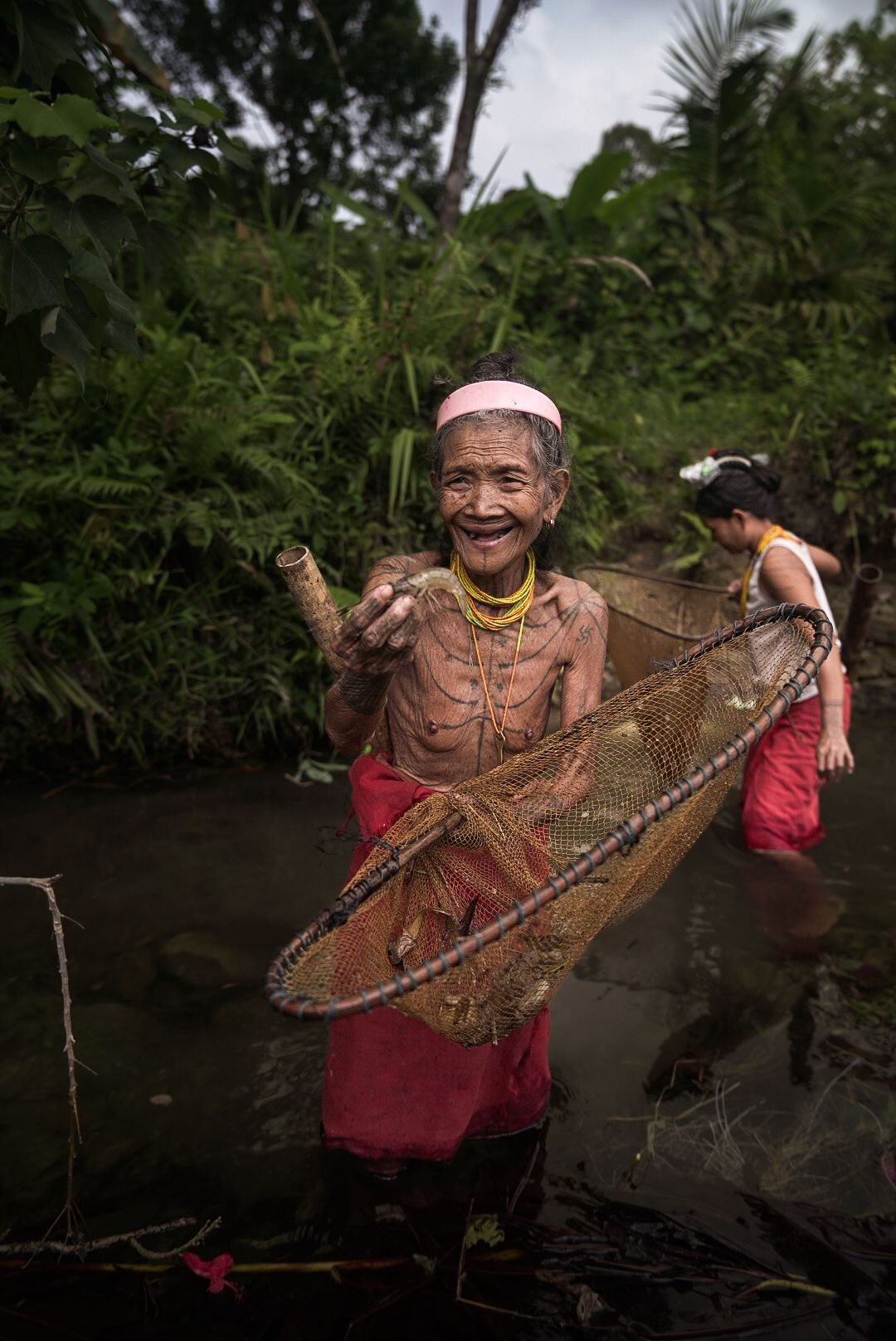 An elderly Mentawai woman catching shrimp with a fishing net