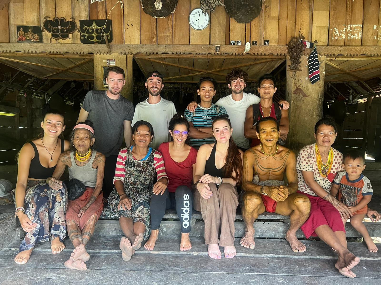 Group of diverse people sitting and standing together in a wooden house, smiling for the camera.