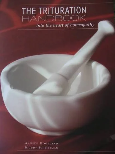 Cover of a book titled 'The Triturations Handbook: into the heart of homeopathy' by Annexe Hogeland & Judy Schreibman, featuring a white mortar and pestle.