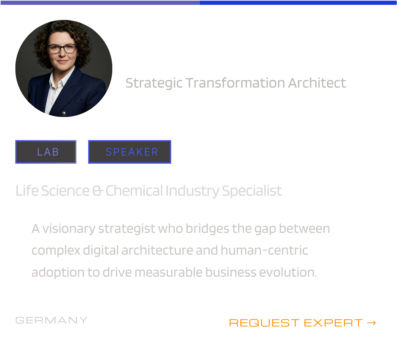 A person with curly hair and glasses wearing a navy blazer and white shirt, smiling. The image appears as a profile picture. The background is dark gray.