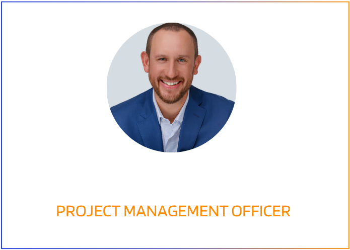 A smiling man in a blue suit and white shirt, with a short beard and bald head, pictured in a digital graphic with colorful design elements.