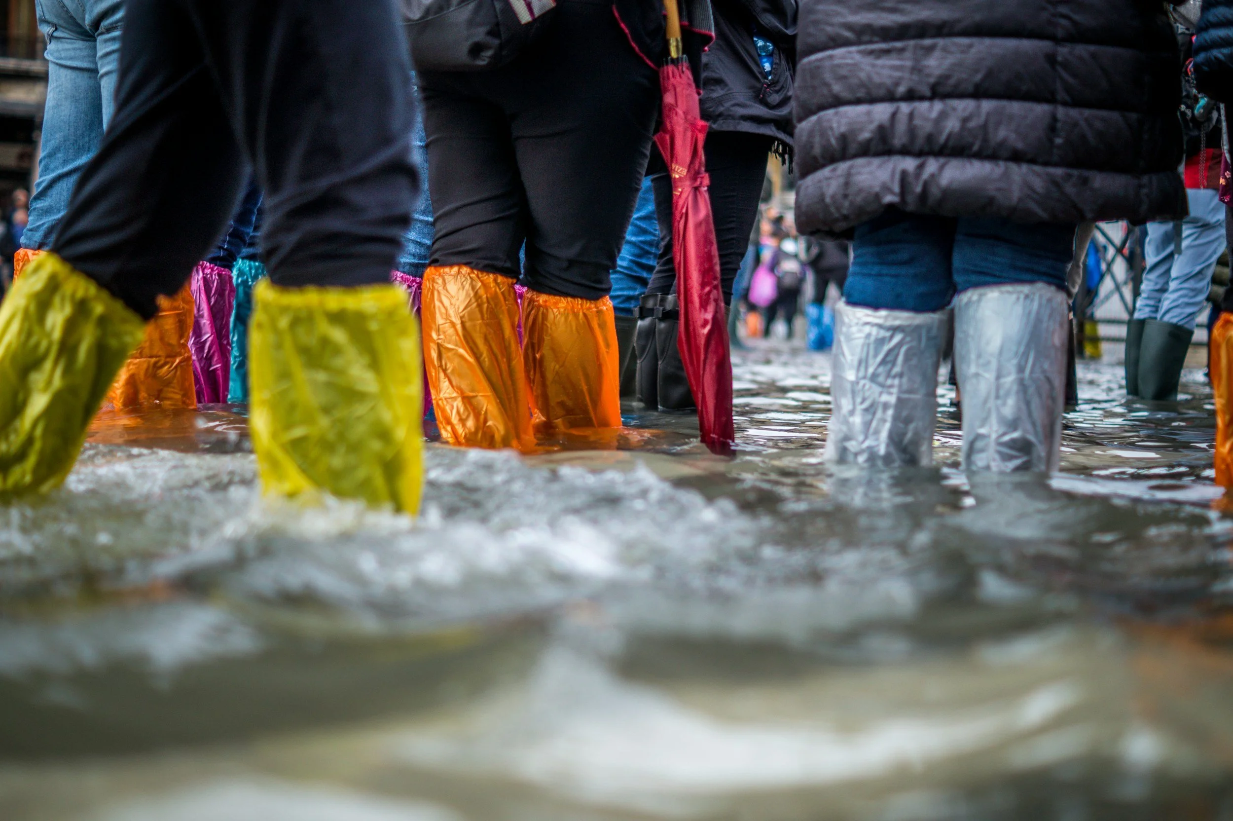 People standing in a flooded street wearing colorful waterproof boots.