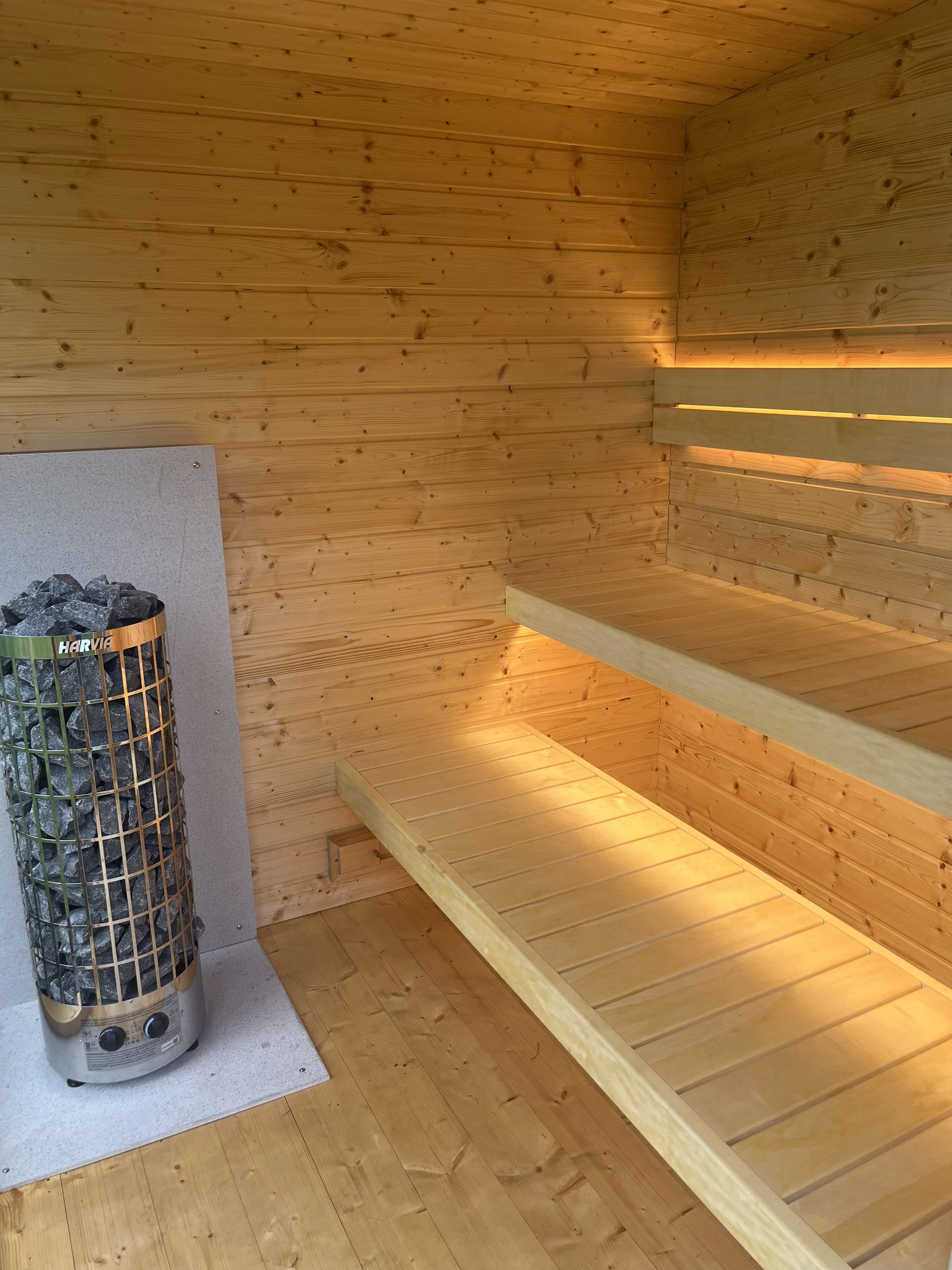 A wooden sauna room with two-tiered wooden benches and a heater filled with stones.