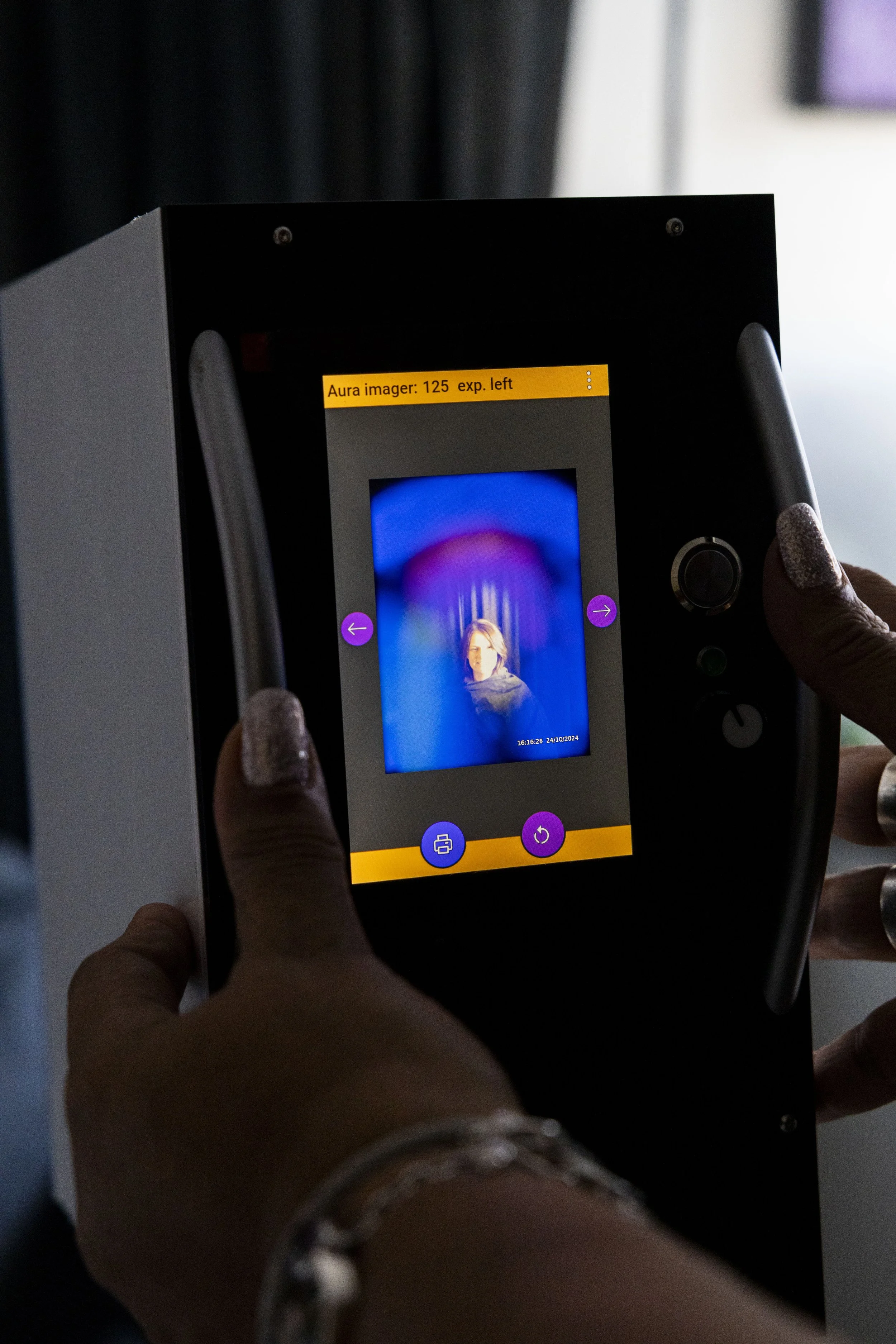 Person holding a digital facial scanner displaying a woman's face on the screen.