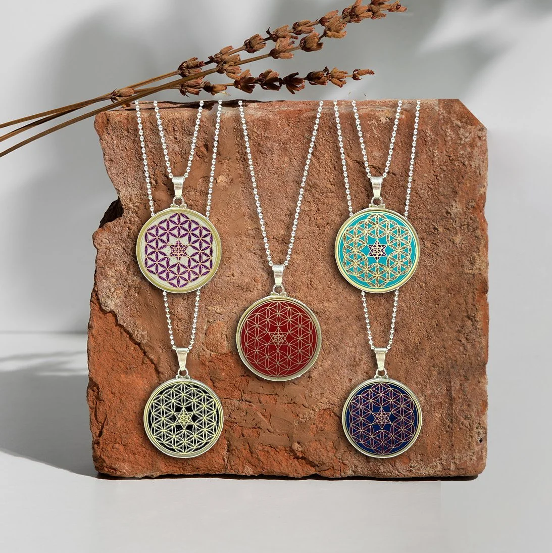 Assorted round pendant necklaces with geometric patterns in various colors, displayed on a brick with dried lavender flowers in the background.
