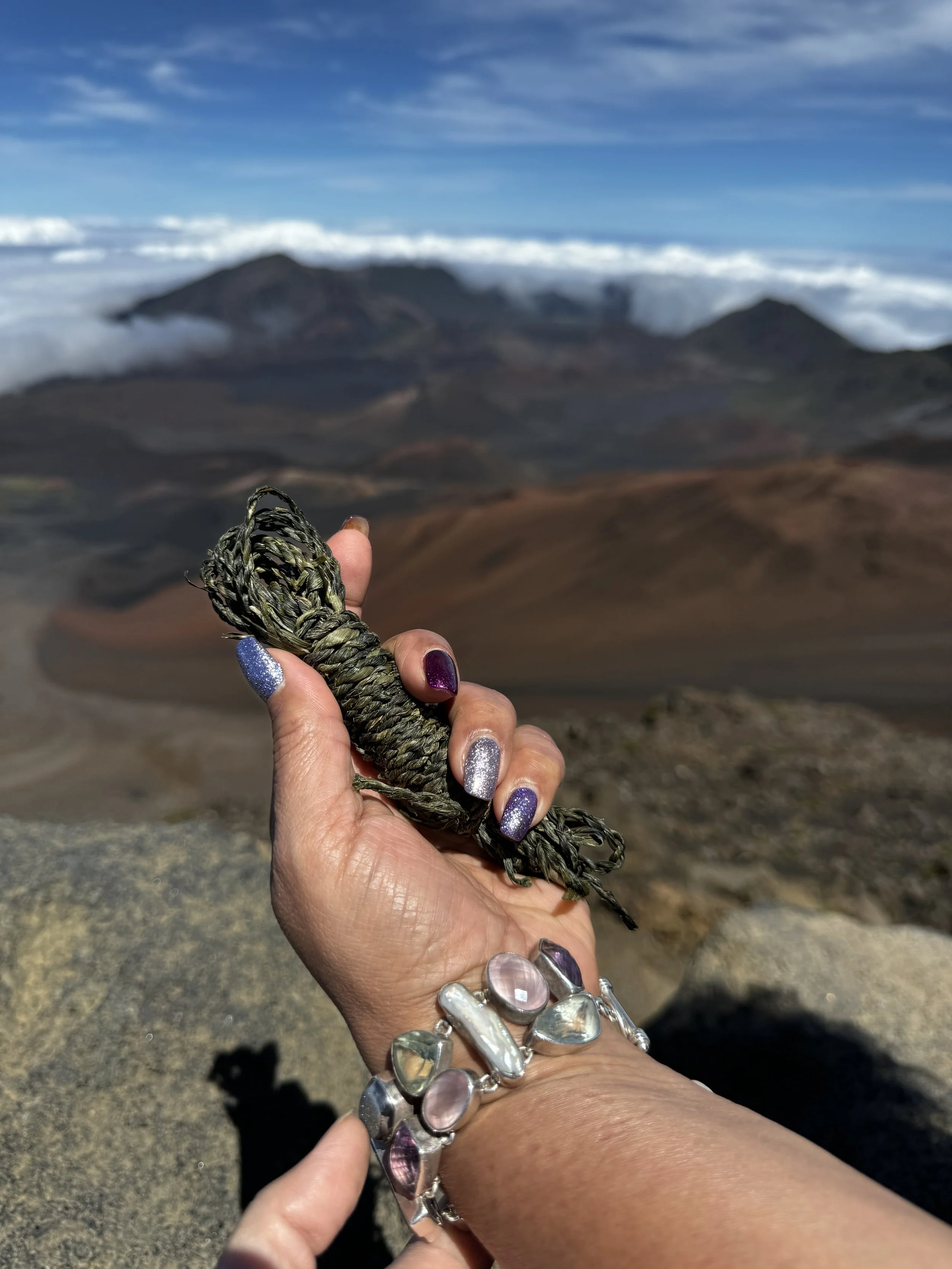 Person holding a braided greenish rope in front of a mountain landscape with clouds and volcanic terrain.