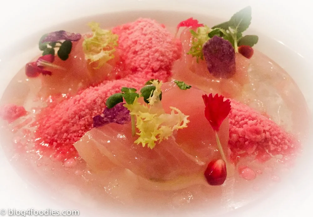 A dessert with pink ice cream, edible flowers, pomegranate seeds, and a light syrup or sauce.