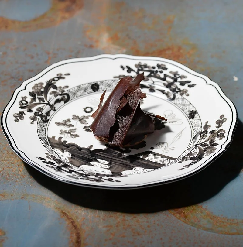 A piece of dark chocolate on a decorative black and white floral plate.