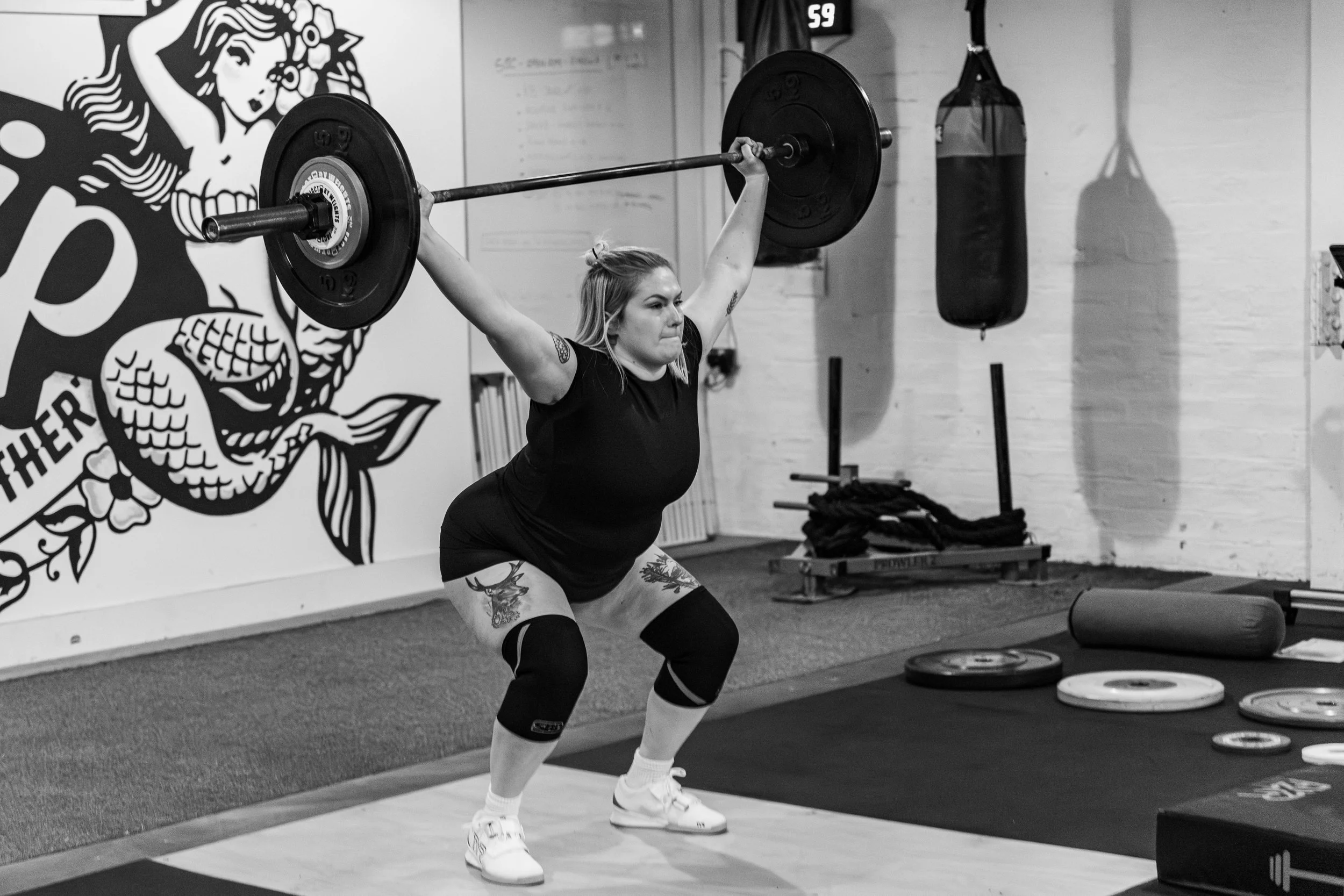 Woman lifting a barbell overhead in a gym.