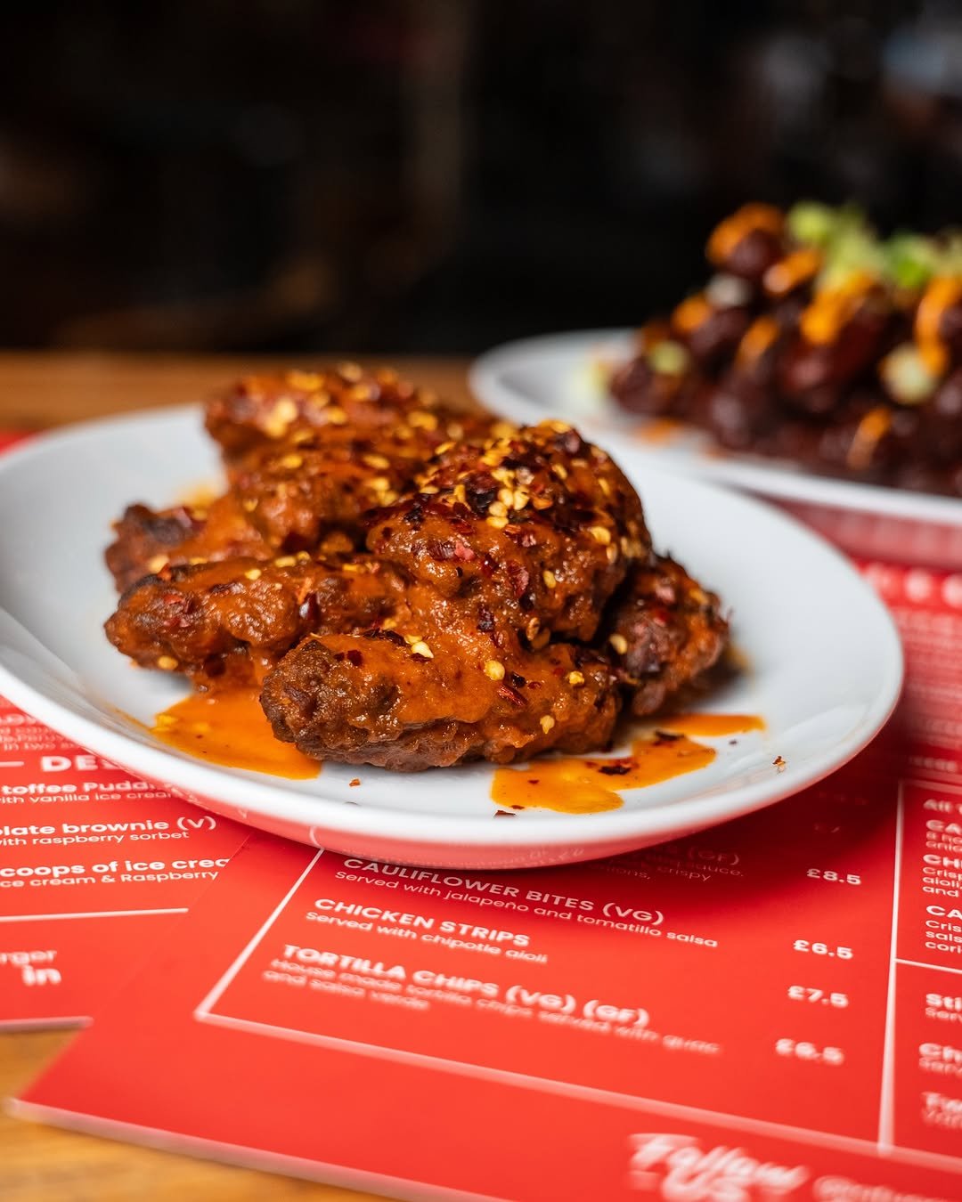 Close-up of spicy glazed chicken drumsticks garnished with chopped herbs and sesame seeds.