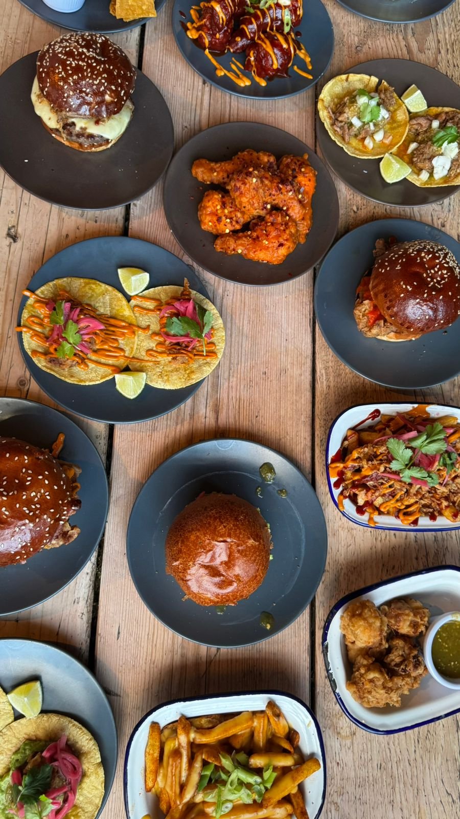 Assortment of Mexican dishes including cheeseburgers, tacos, fried chicken, and sides on a wooden table.