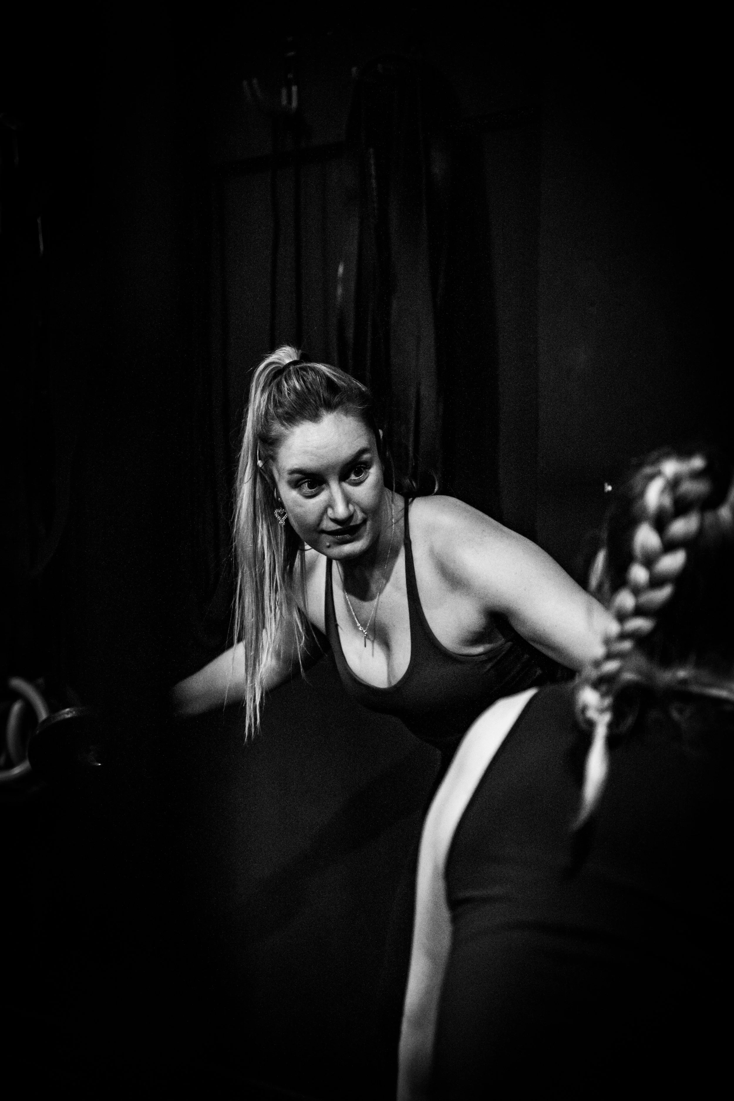 A black and white photo of a woman with a high ponytail and a tank top, working out with a dumbbell in a gym, focused on her resistance training.