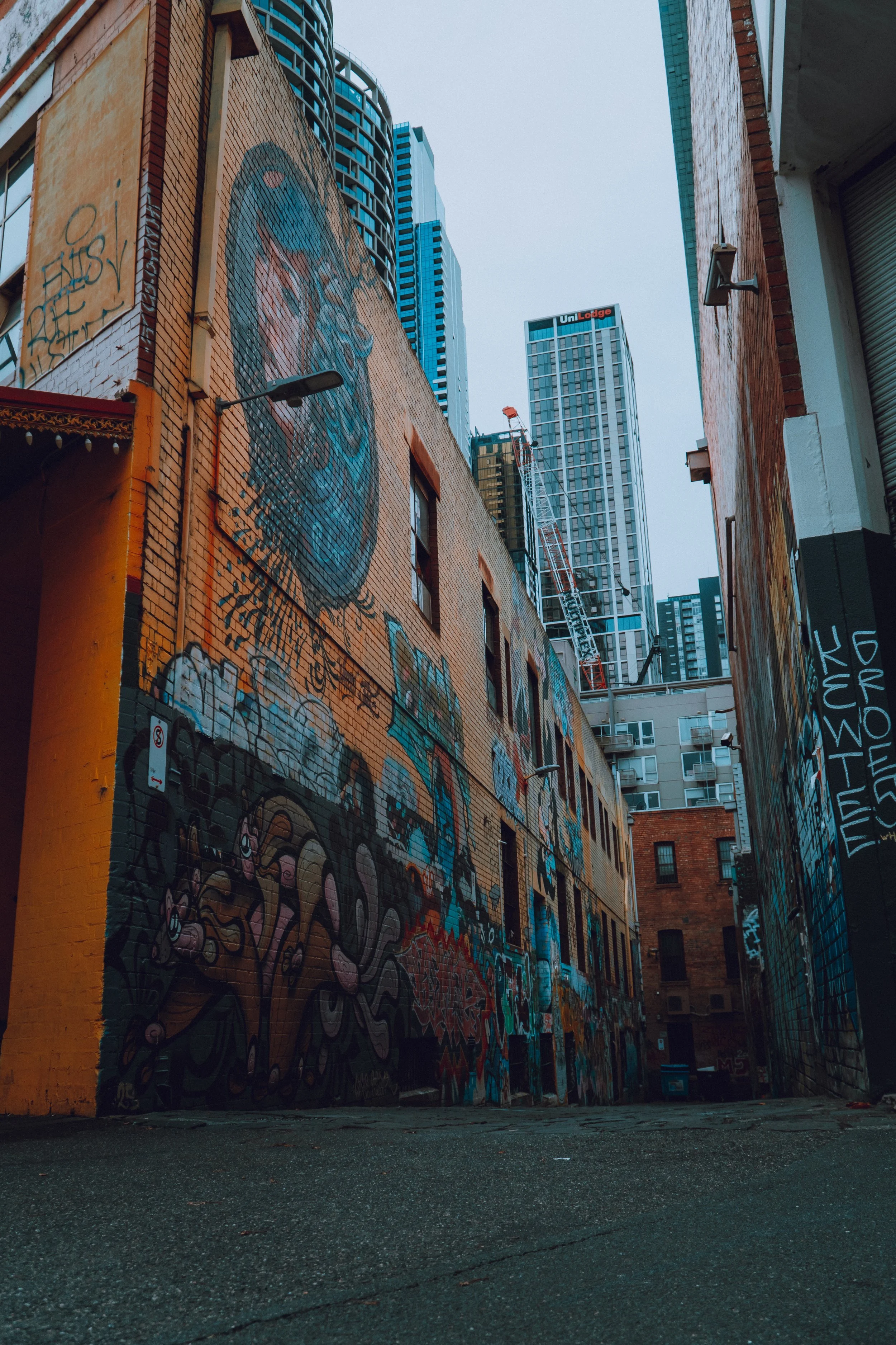 Urban alleyway with brick buildings, graffiti art, and tall modern skyscrapers in the background.