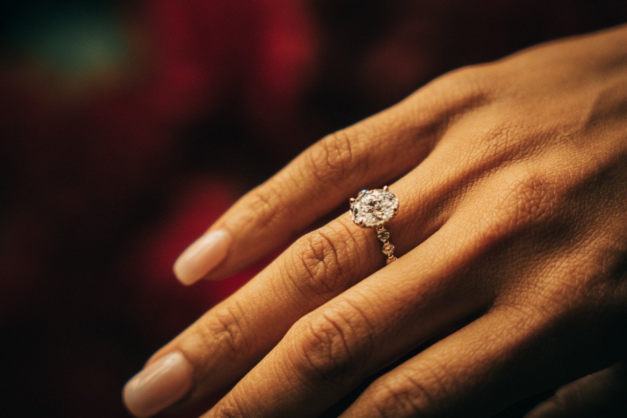 Close-up of a person's hand with a diamond engagement ring on the ring finger.