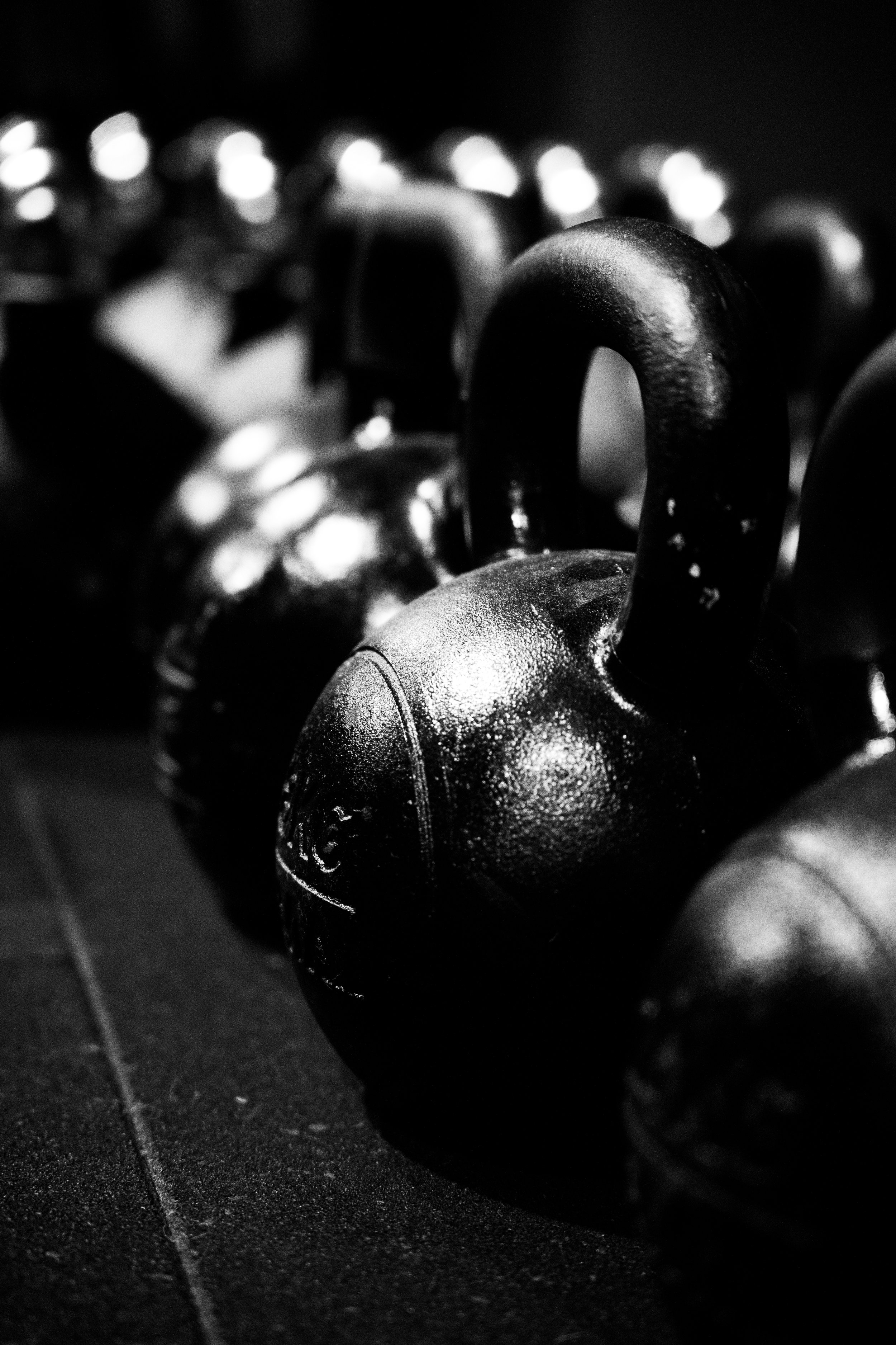 Close-up of several black kettlebells arranged in a row in a gym, with a textured surface and metallic highlights, in black and white.