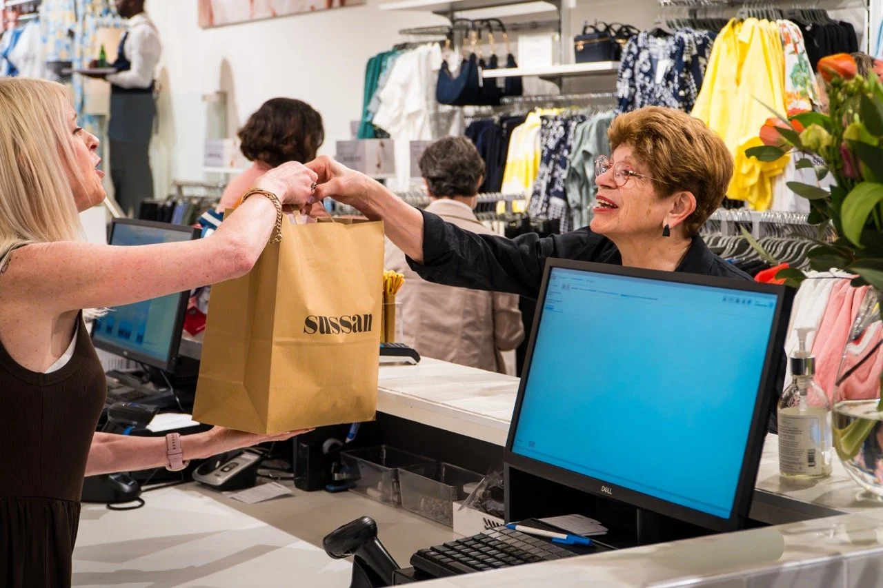 Customer receiving a shopping bag from a cashier at a clothing store checkout counter.