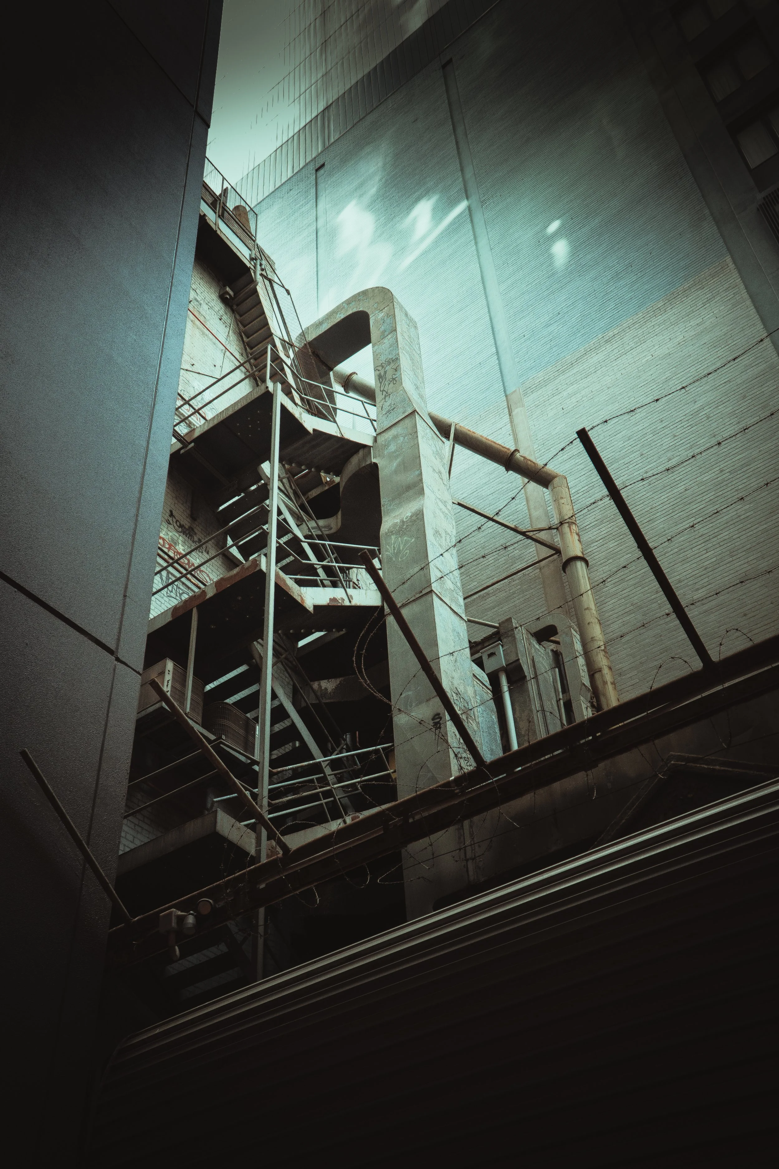 An outdoor fire escape stairwell on the side of a tall building with modern concrete and metal architecture.
