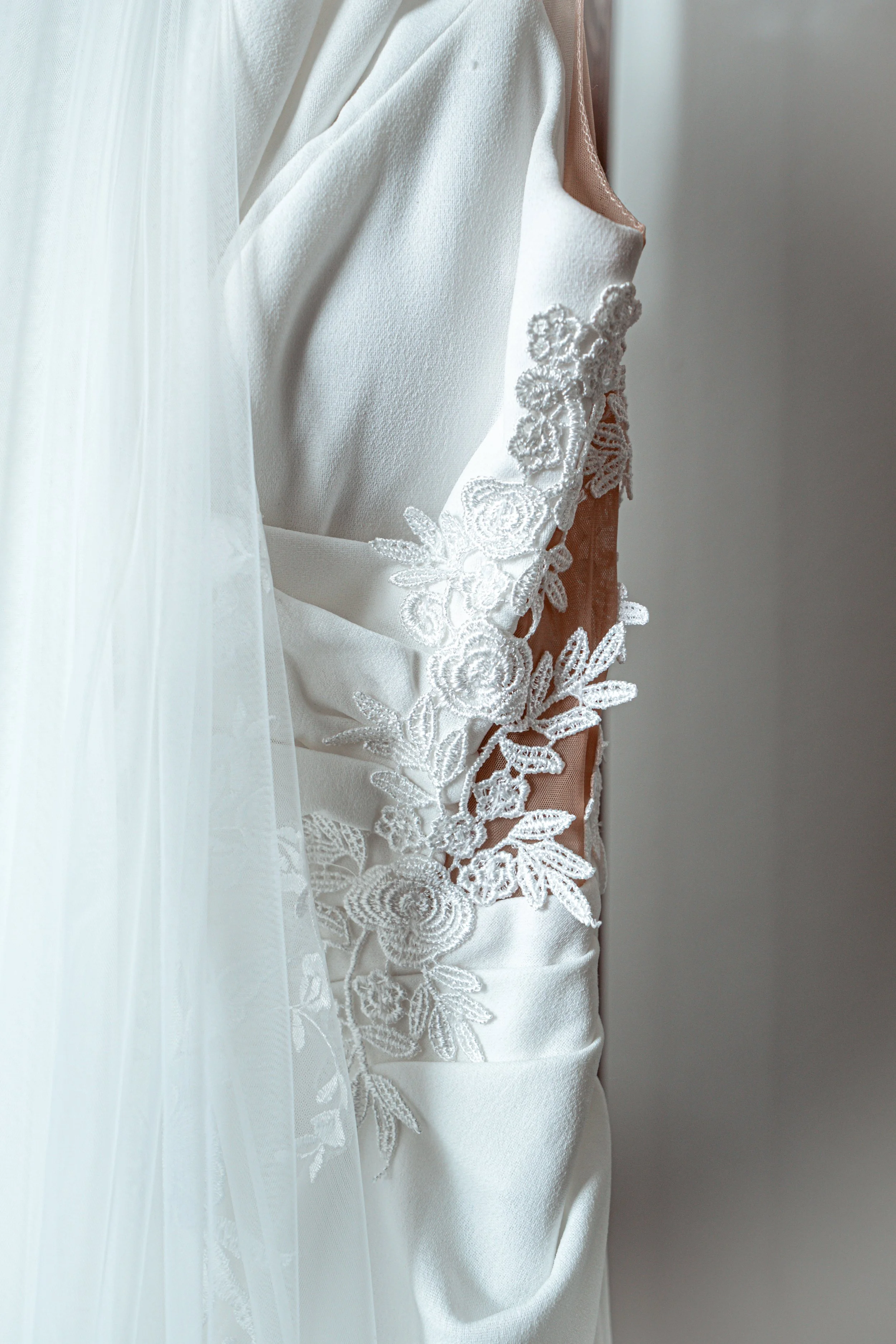 Close-up of a white wedding dress with lace floral embroidery on the side.