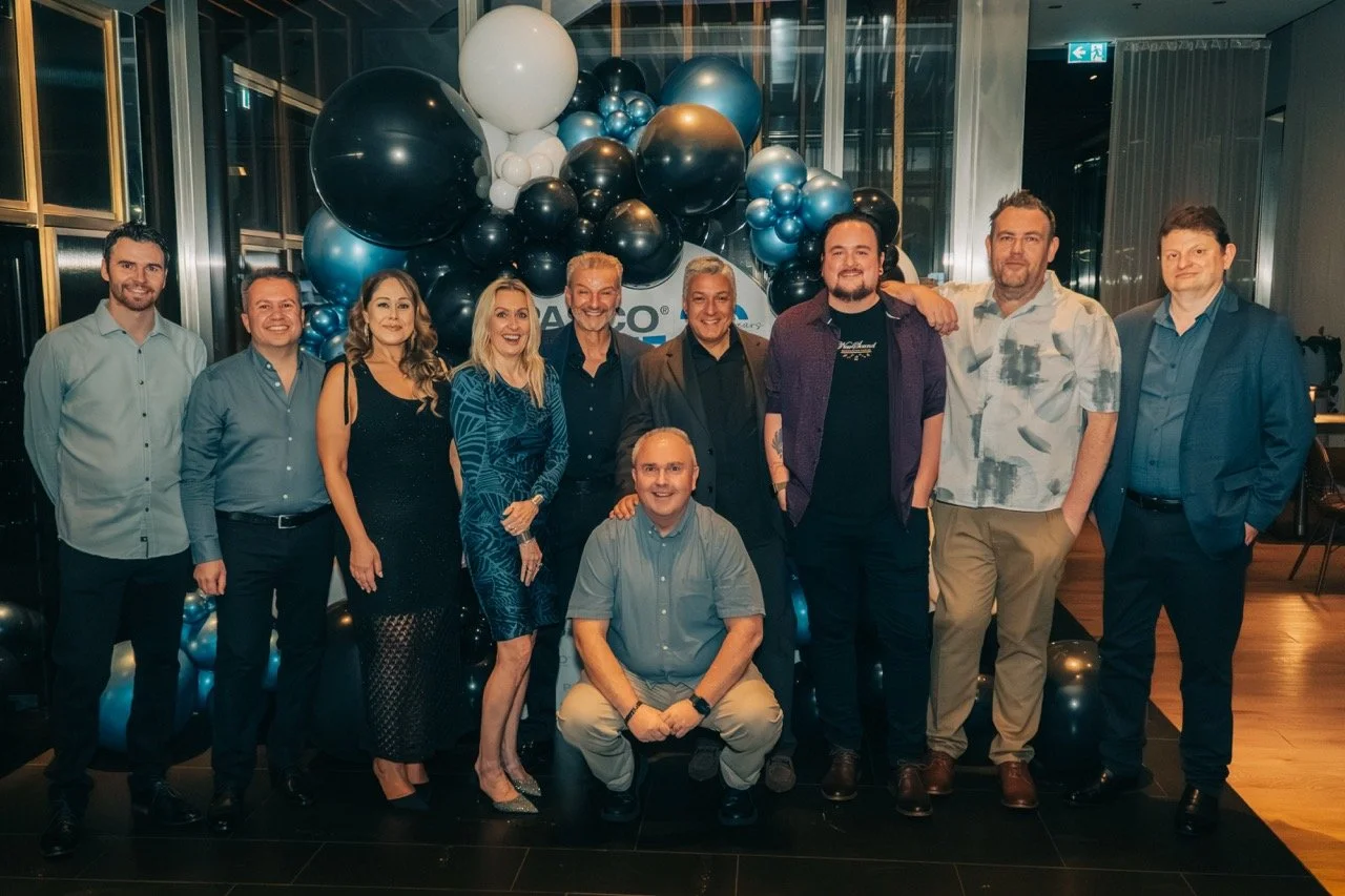 Group of ten people posing in front of a balloon display at an event or celebration.