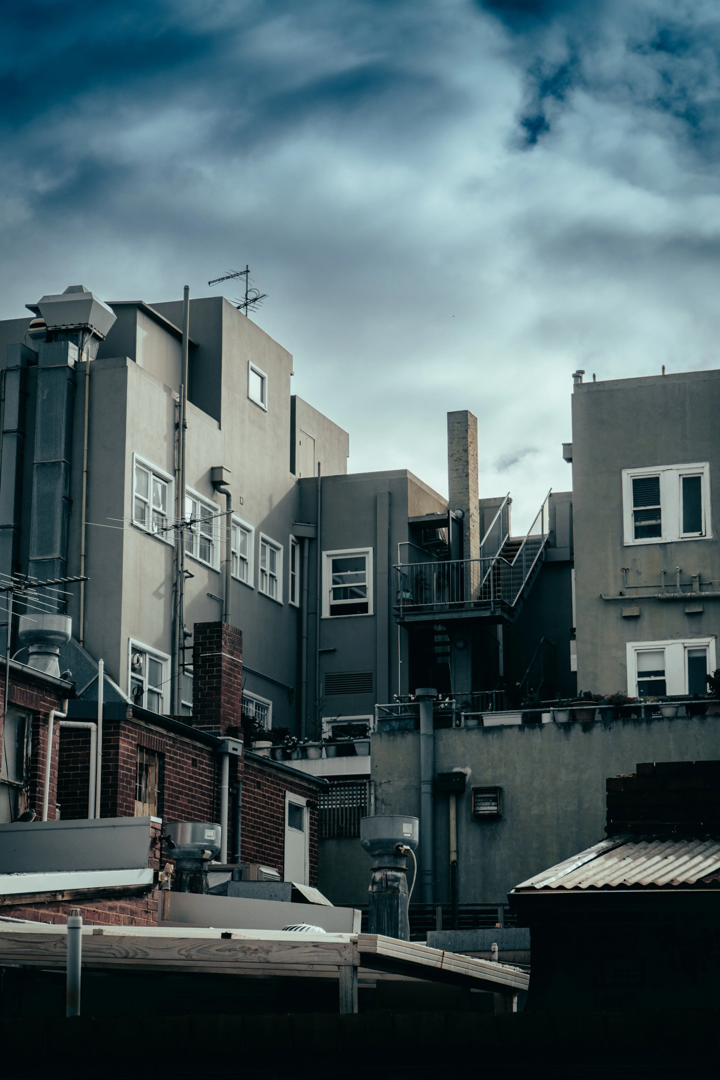 Cityscape showing multi-story buildings with various windows, vents, and chimneys under a cloudy sky.