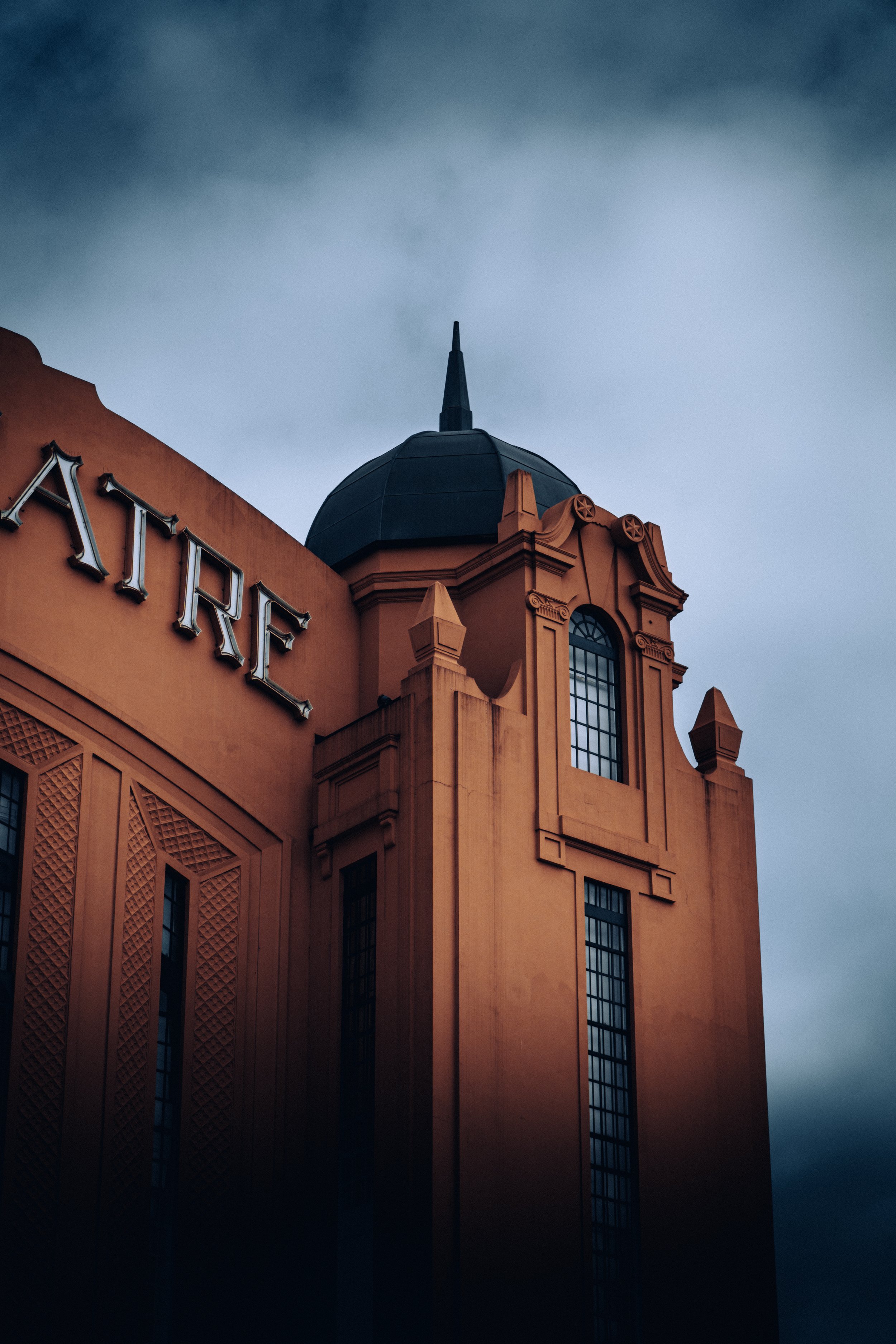 Close-up of a building with Art Deco architectural style, featuring a rounded tower with a spire on top, and the word 'ART' partially visible on the facade, under a cloudy sky.