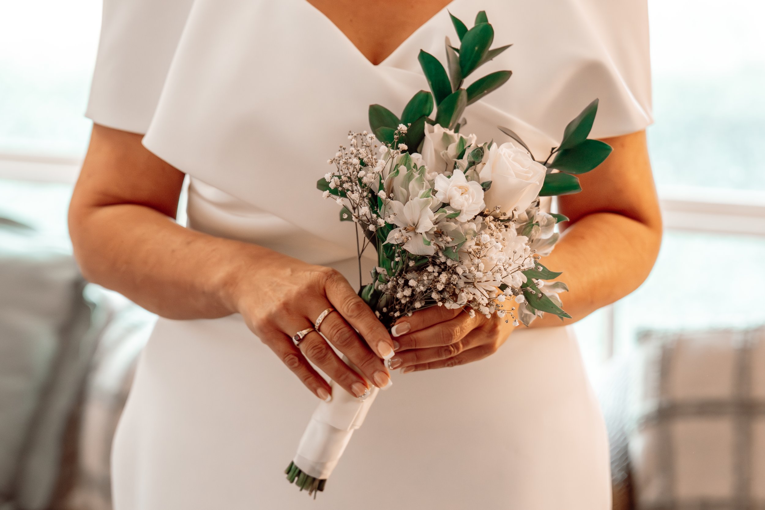 A woman in a white dress holding a bouquet of white roses, lilies, baby's breath, and greenery.