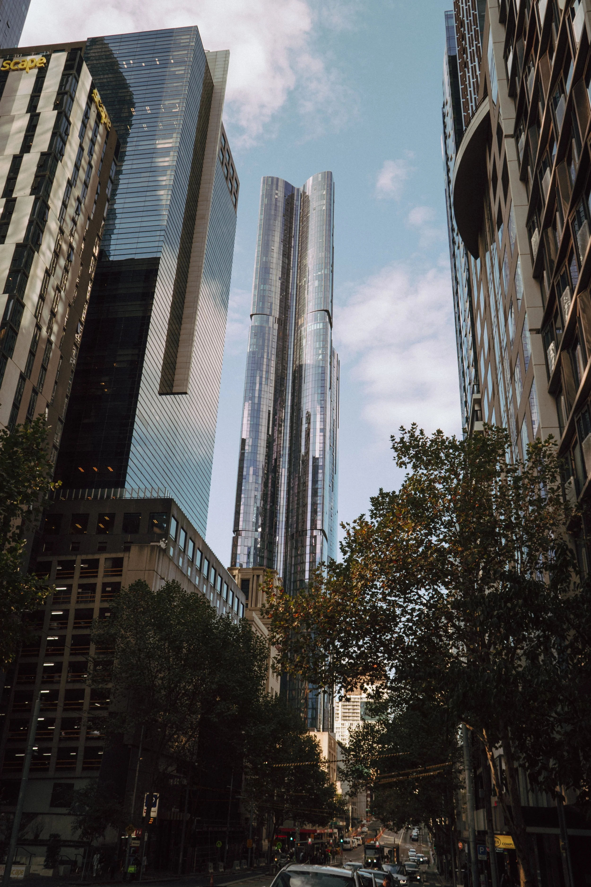 Tall modern skyscrapers in a city, with trees and a busy street below.