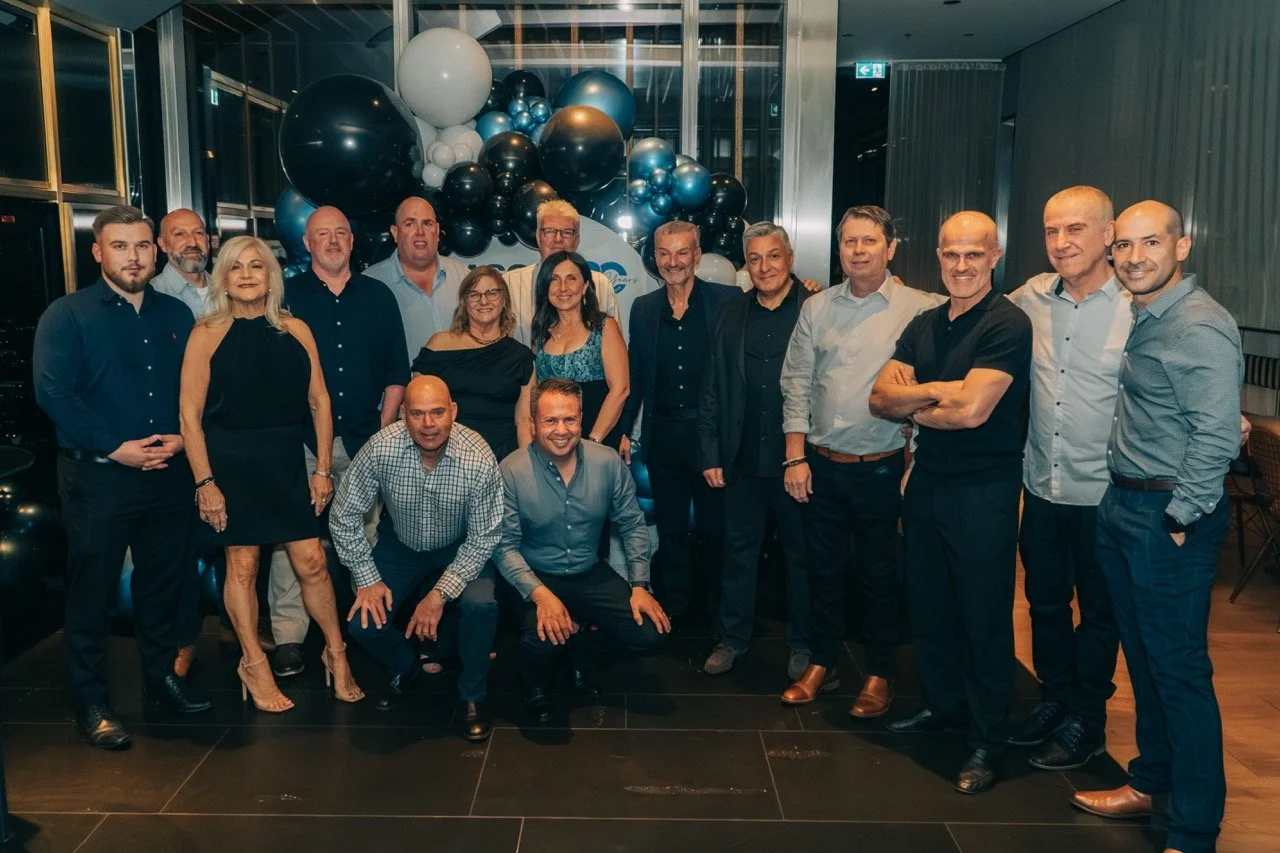 Group of people posing for a photo at a celebration or event, with black, white, and blue balloons in the background.
