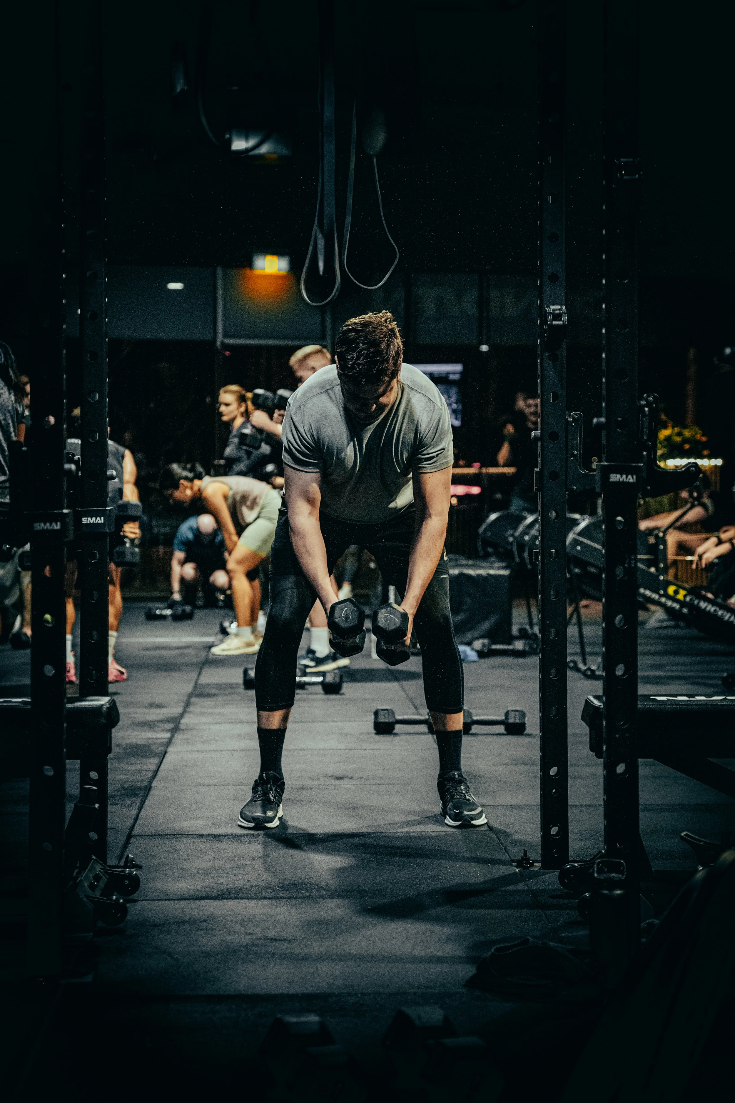 Person lifting dumbbells in a gym with other people working out in the background.