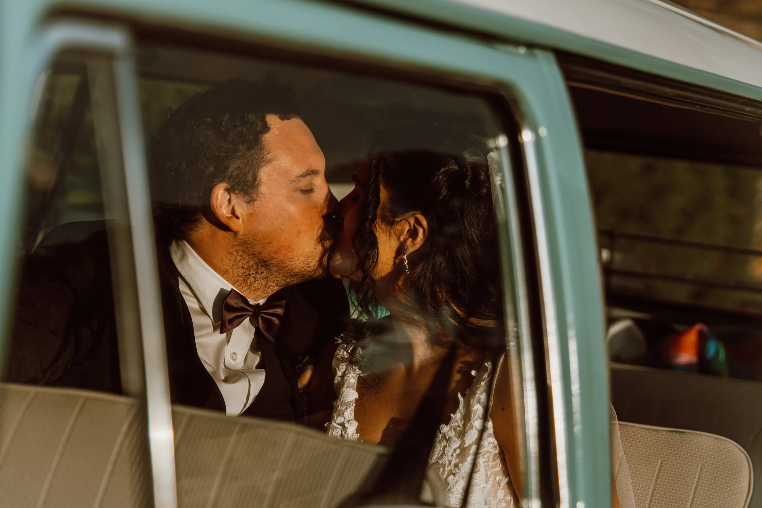 A couple dressed in formal wedding attire sharing a kiss inside a classic car.